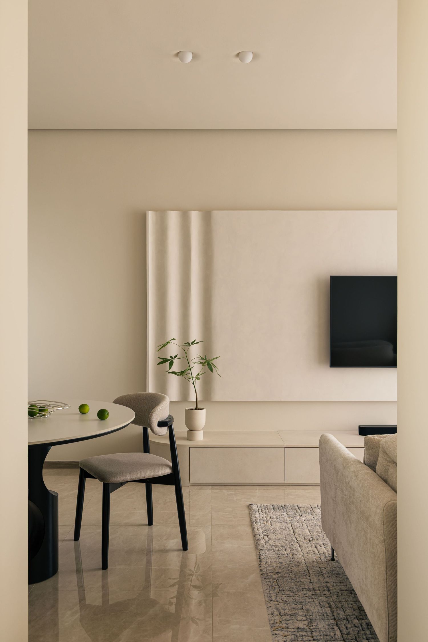 Minimalist beige living and dining area with TV wall panel, round table, modern chairs, and neutral decor.