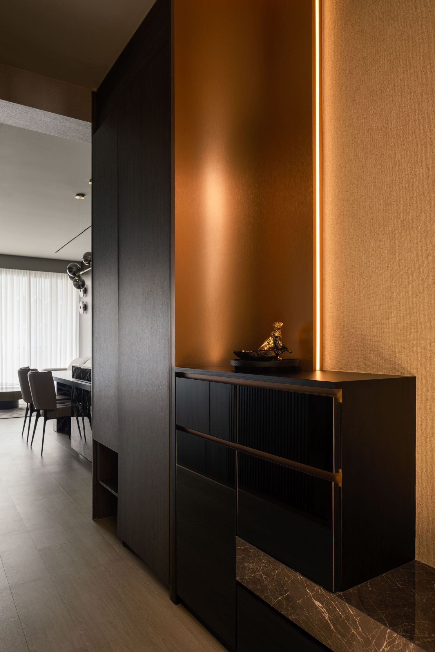 Luxury entryway with black floating cabinet, warm copper accent wall, vertical LED strip lighting, and marble base in modern interior.