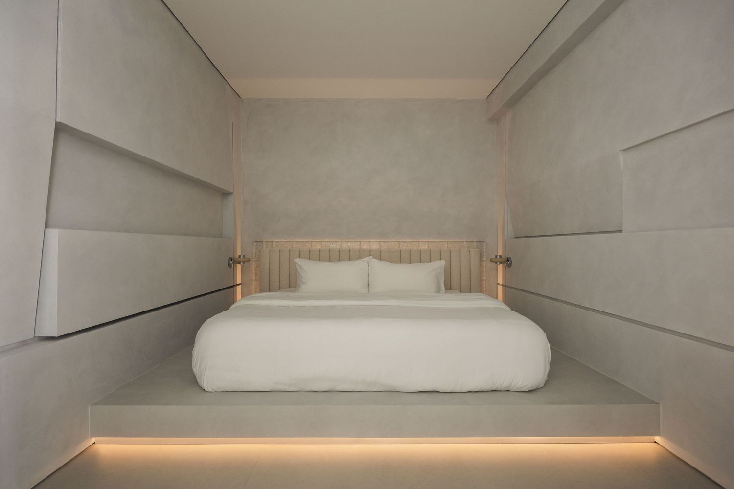 Modern minimalist bedroom with white bedding, LED-lit platform bed, and neutral gray walls with built-in shelving.