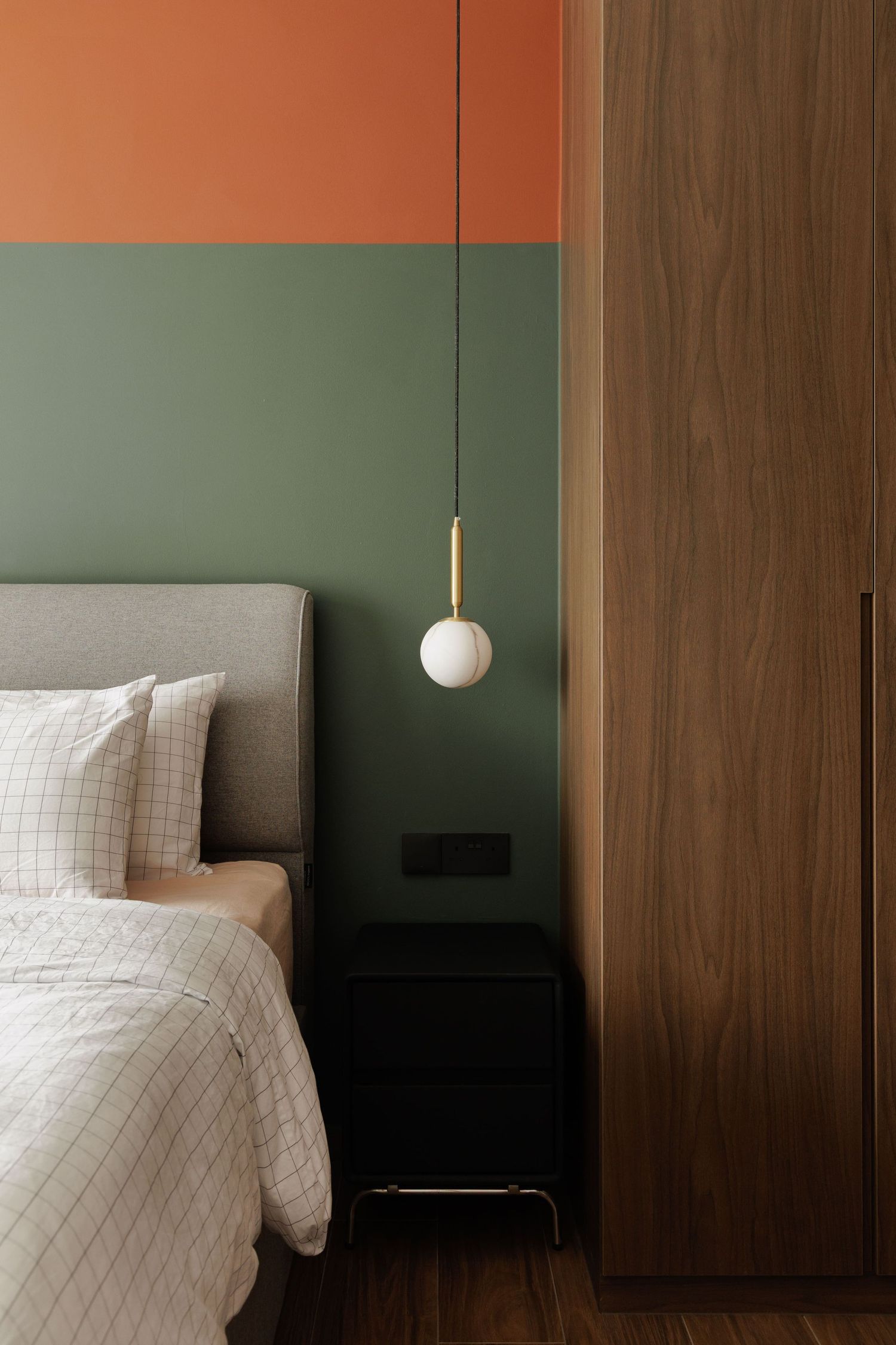 Modern bedroom interior with green walls, wooden panels, and minimalist pendant lighting fixture against textured wall.
