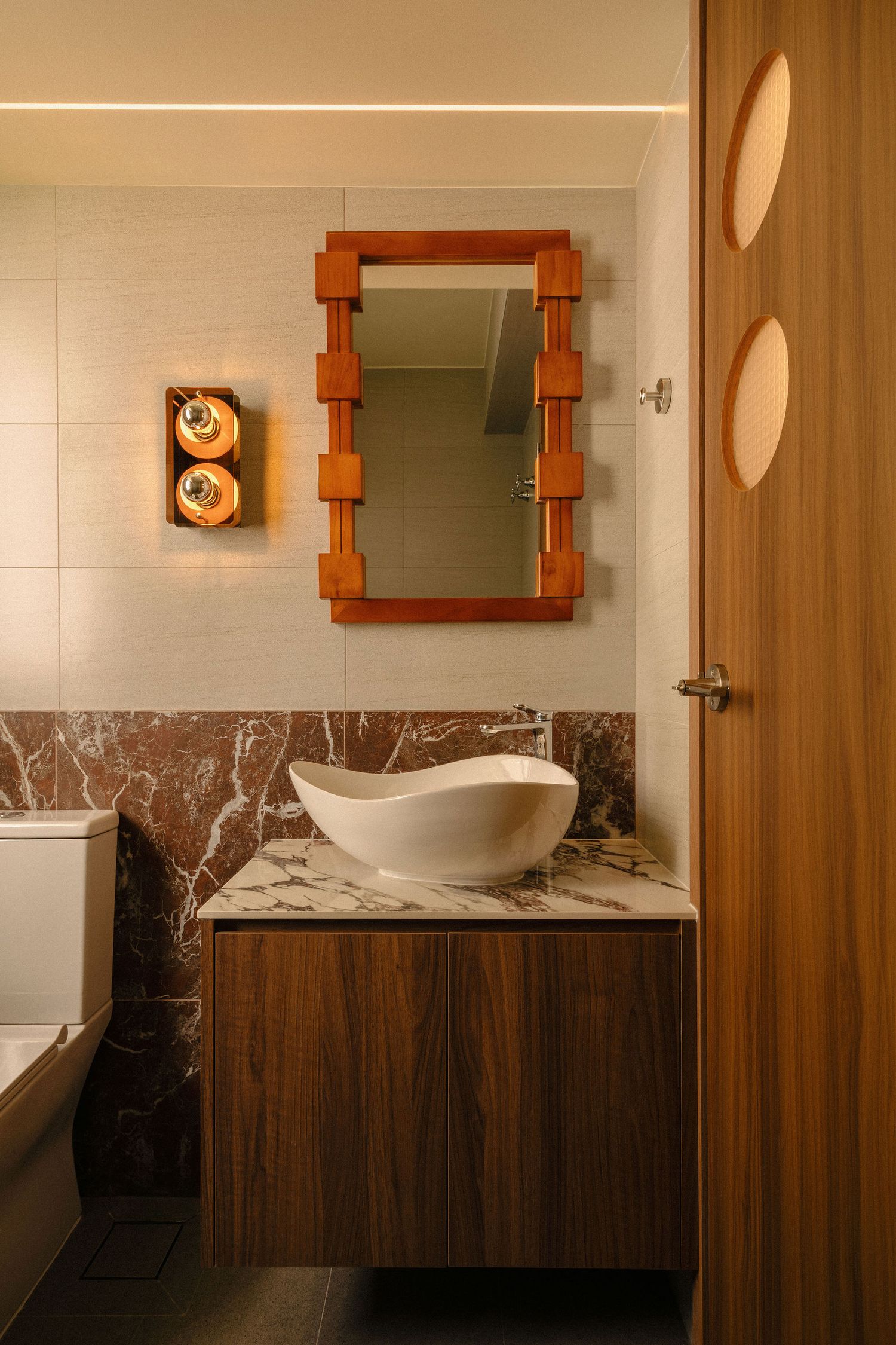 Modern bathroom with a white vessel sink, floating walnut vanity, red marble backsplash, wood-framed mirror, retro wall sconce and wooden do