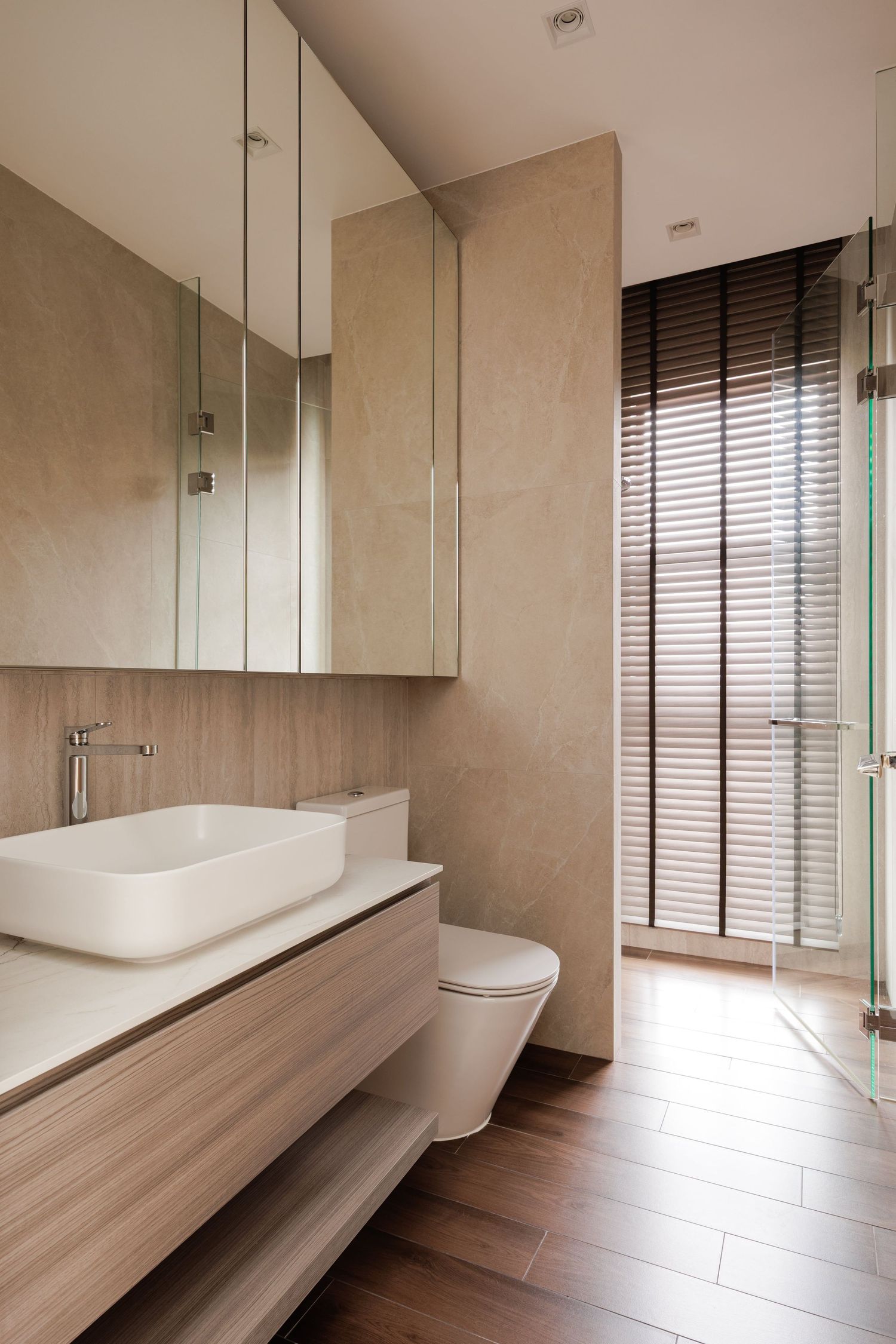 A modern bathroom features a sleek built-in wooden bench and clean white fixtures with minimalist beige walls and flooring.