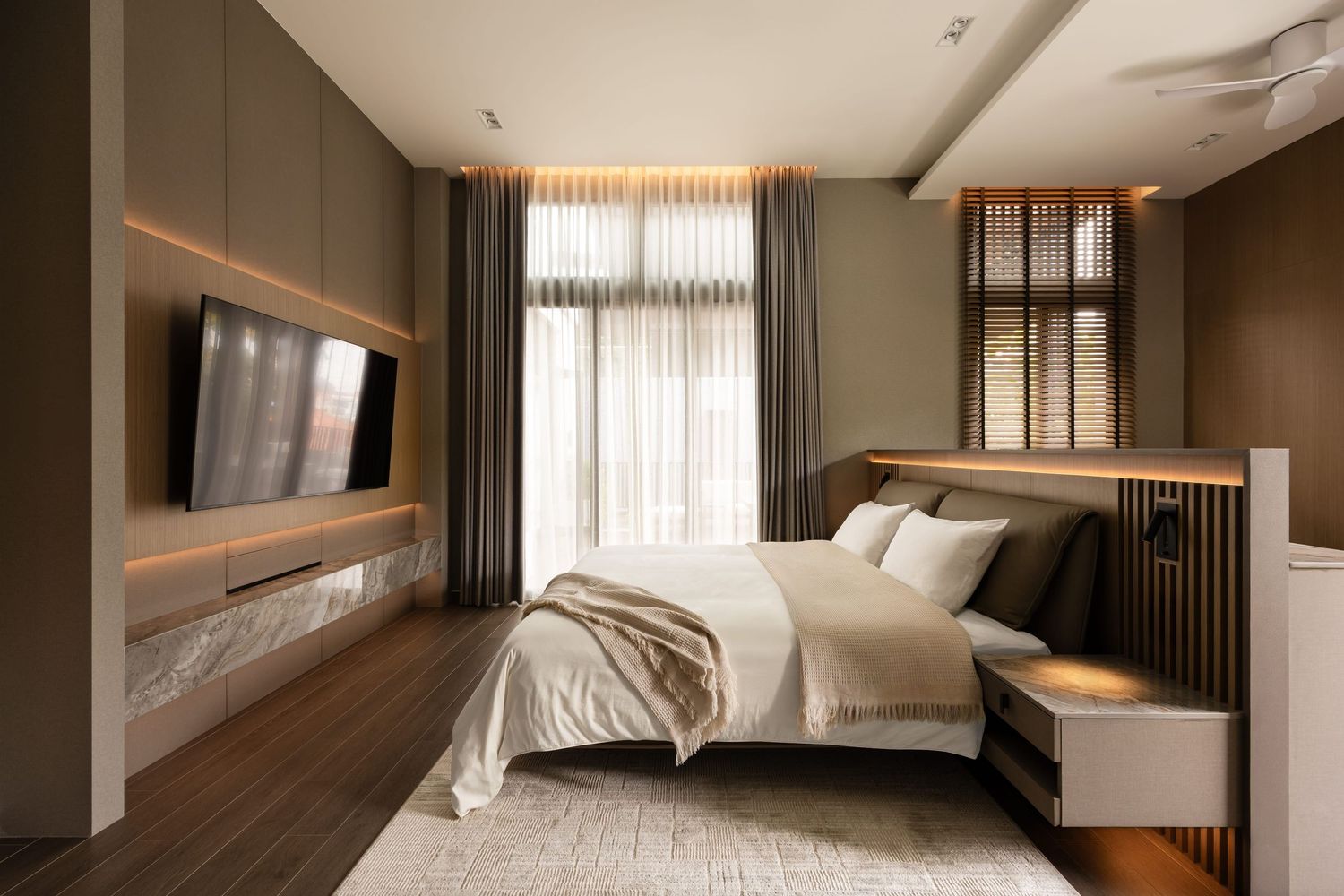 Modern luxurious hotel room with dual sunlit windows, wooden flooring, and contemporary furnishings in warm tones.