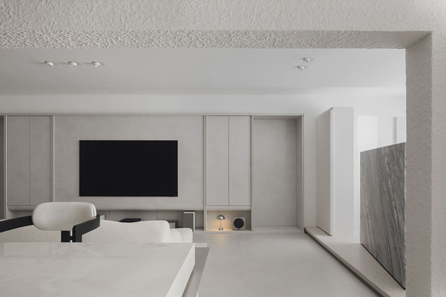Minimalist living room with wall-mounted TV, neutral gray cabinetry, white furniture, and clean modern design.