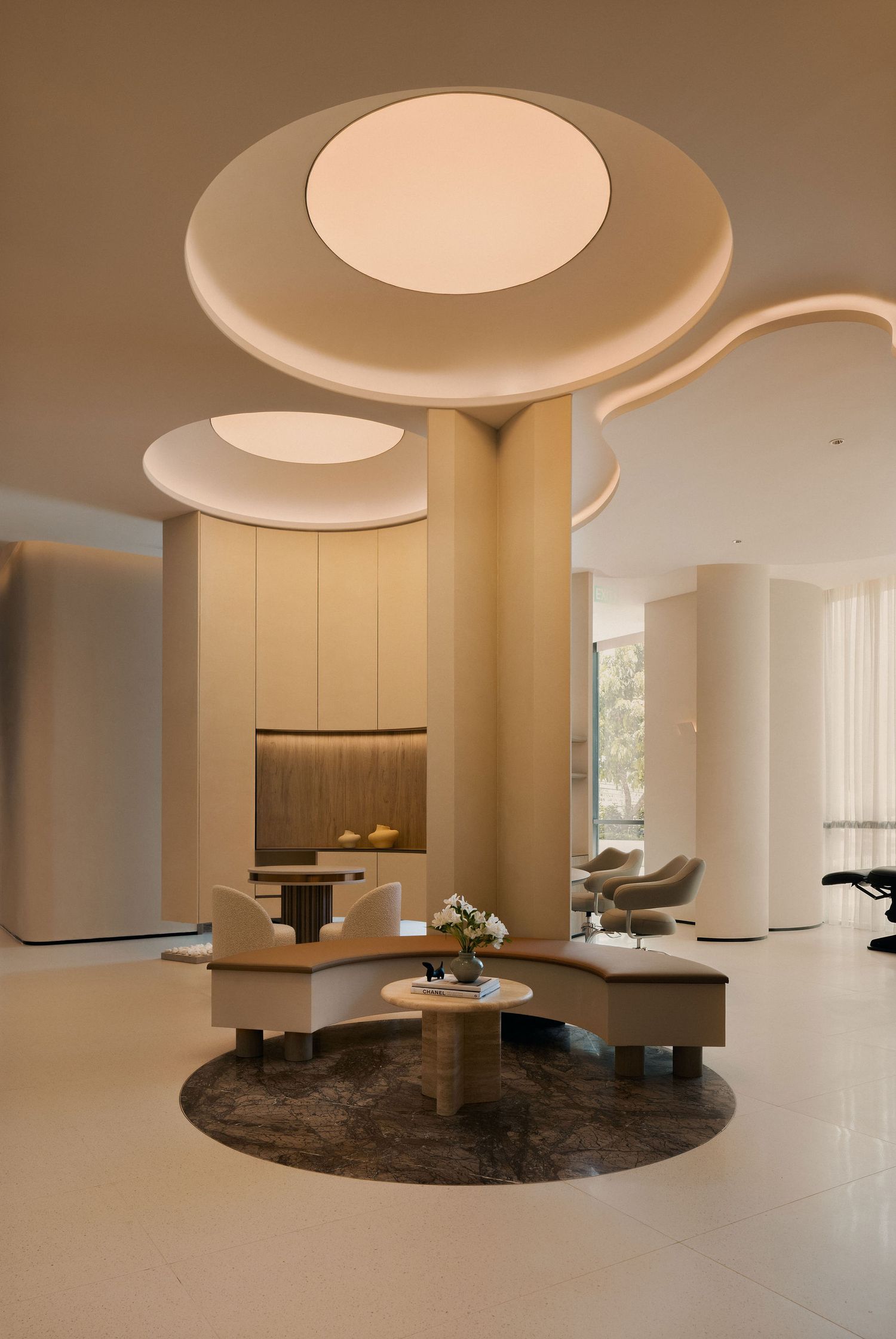 Modern hotel lobby with circular ceiling lights, cylindrical columns, and elegant seating arrangement on a dark marble rug.