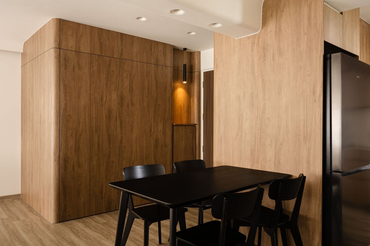 Modern dining area with black chairs and wooden paneled walls featuring recessed lighting and hanging pendant lamps.
