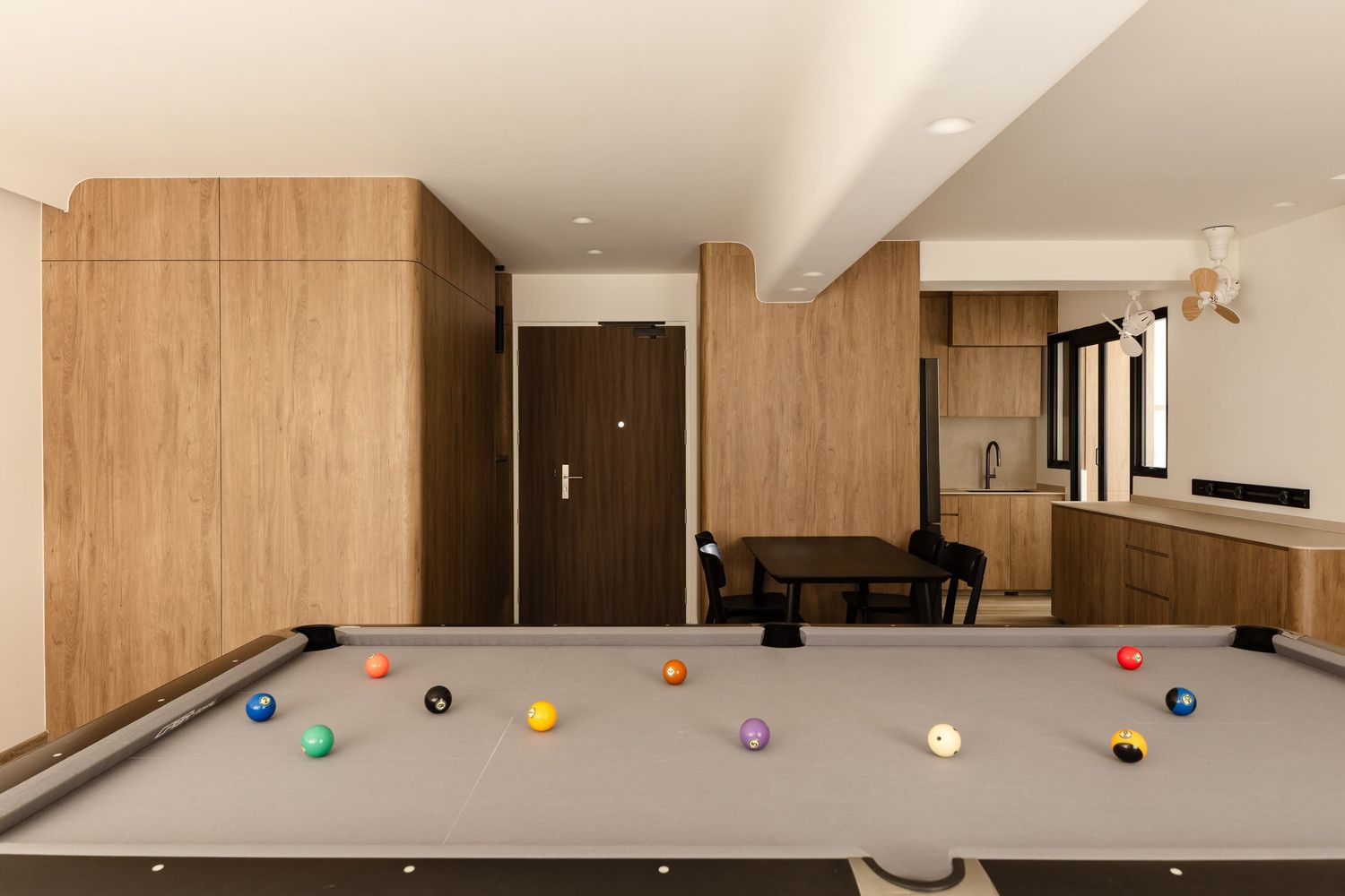Modern recreation room interior with pool table and colorful billiard balls scattered on gray felt surface.