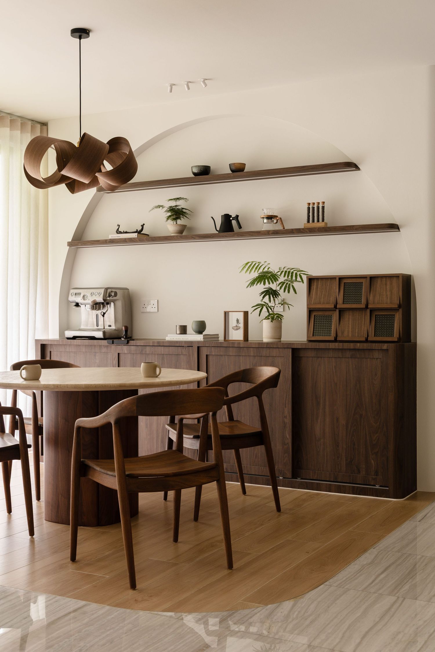 Modern dining area with dark wood furniture, floating shelves, and contemporary pendant lighting in a minimalist interior space.