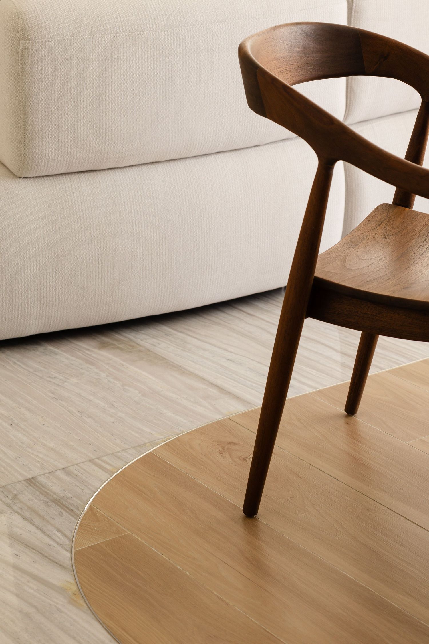 Close-up view of modern wooden dining chairs and white sofa on light hardwood flooring in contemporary living space.