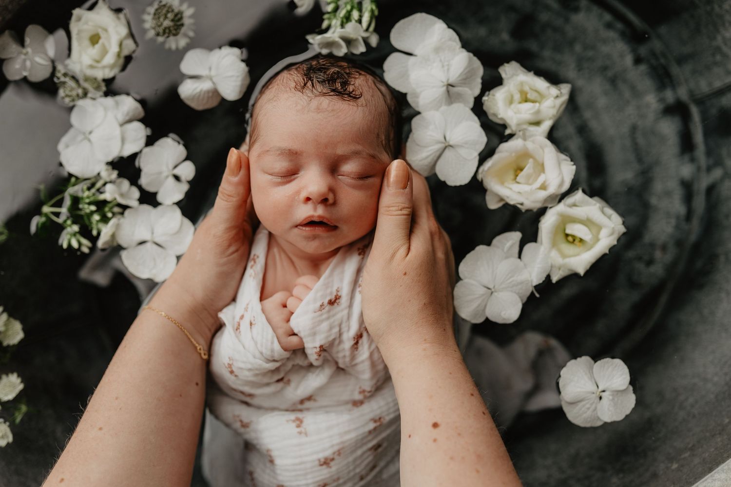 Un nouveau-né endormi dans un bain fleuri entouré de délicates fleurs de roses blanches repose doucement dans les mains.