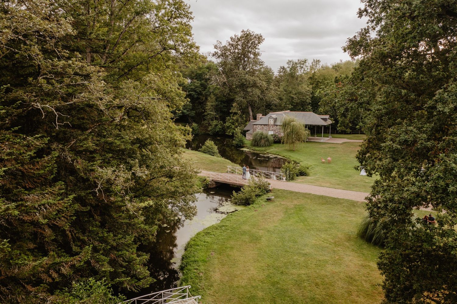 Photo aérienne de marier sur un pont d'une pelouse bien entretenue nichée parmi les arbres au bord d'un ruisseau au domaine 
des longrais