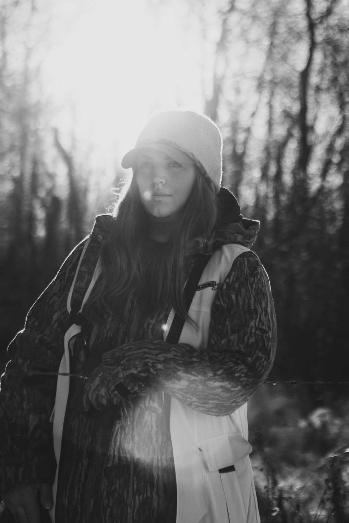 Winter portrait in black and white showing a person wearing a beanie and winter coat in the forest.