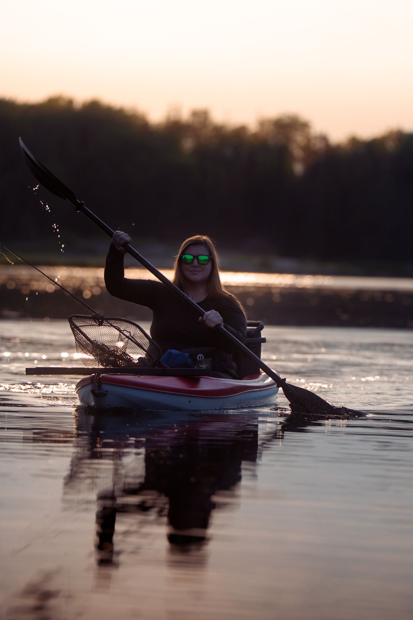 Silhouetted kayaker paddling on calm water at sunset with reflections on the lake surface.