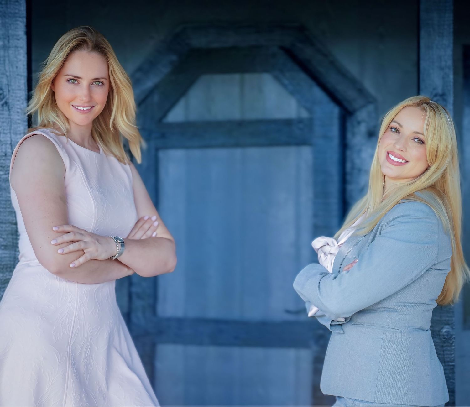 Two smiling blonde women in elegant attire pose with arms crossed in front of blue backdrop.