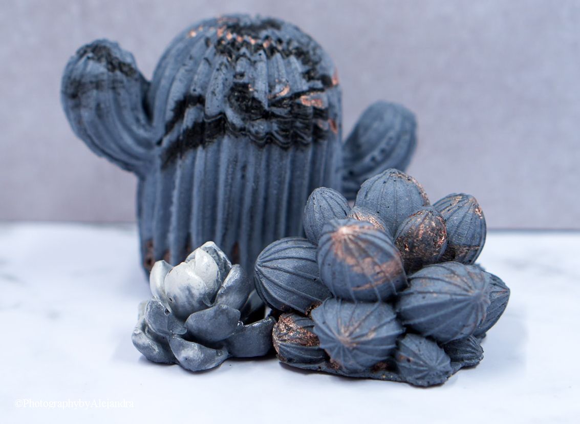 Dark blue concrete cactus and succulent sculptures with copper accents on white marble surface.