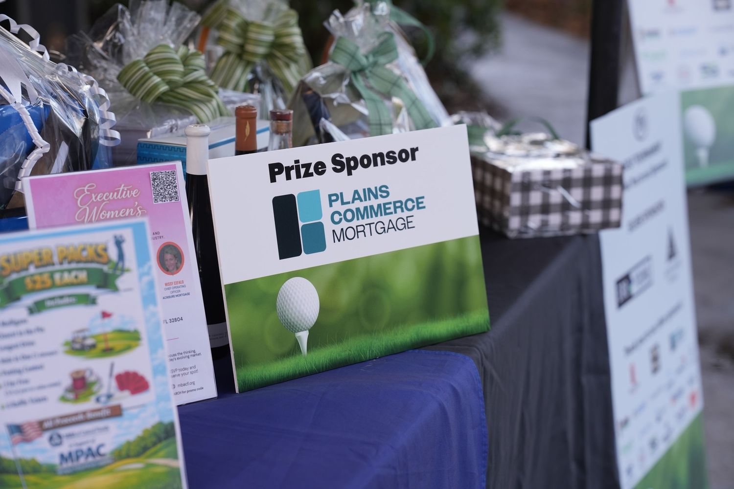 Plains Commerce Mortgage prize sponsor sign displayed at golf tournament registration table.