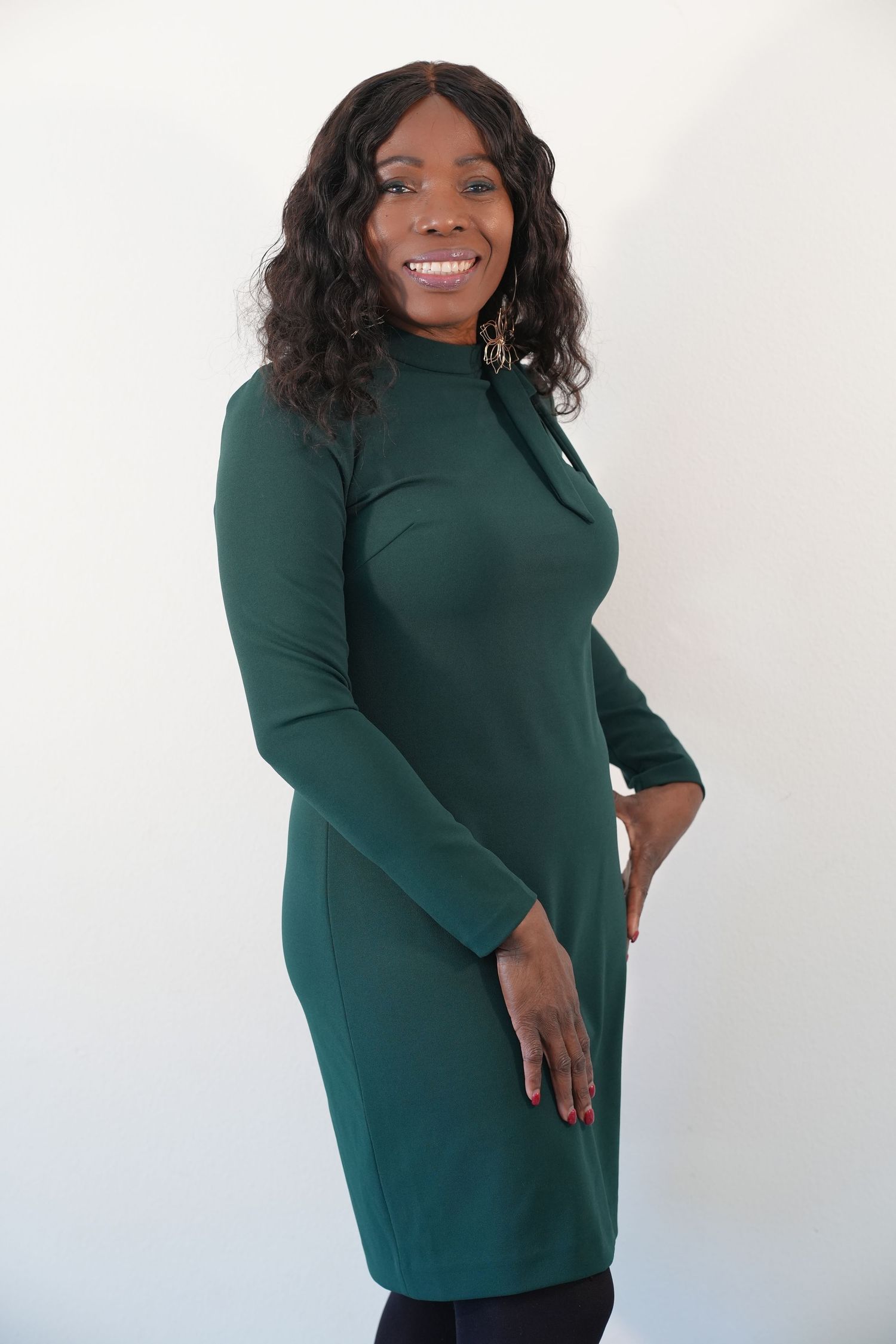 Smiling woman in forest green turtleneck dress poses confidently against white background.