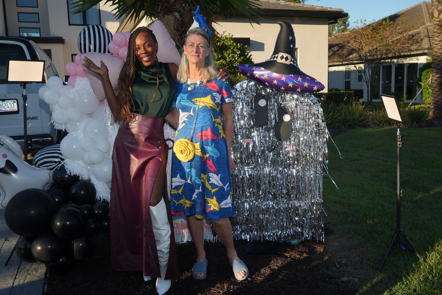 Two women in Halloween costumes posing outdoors with festive yard decorations at night.