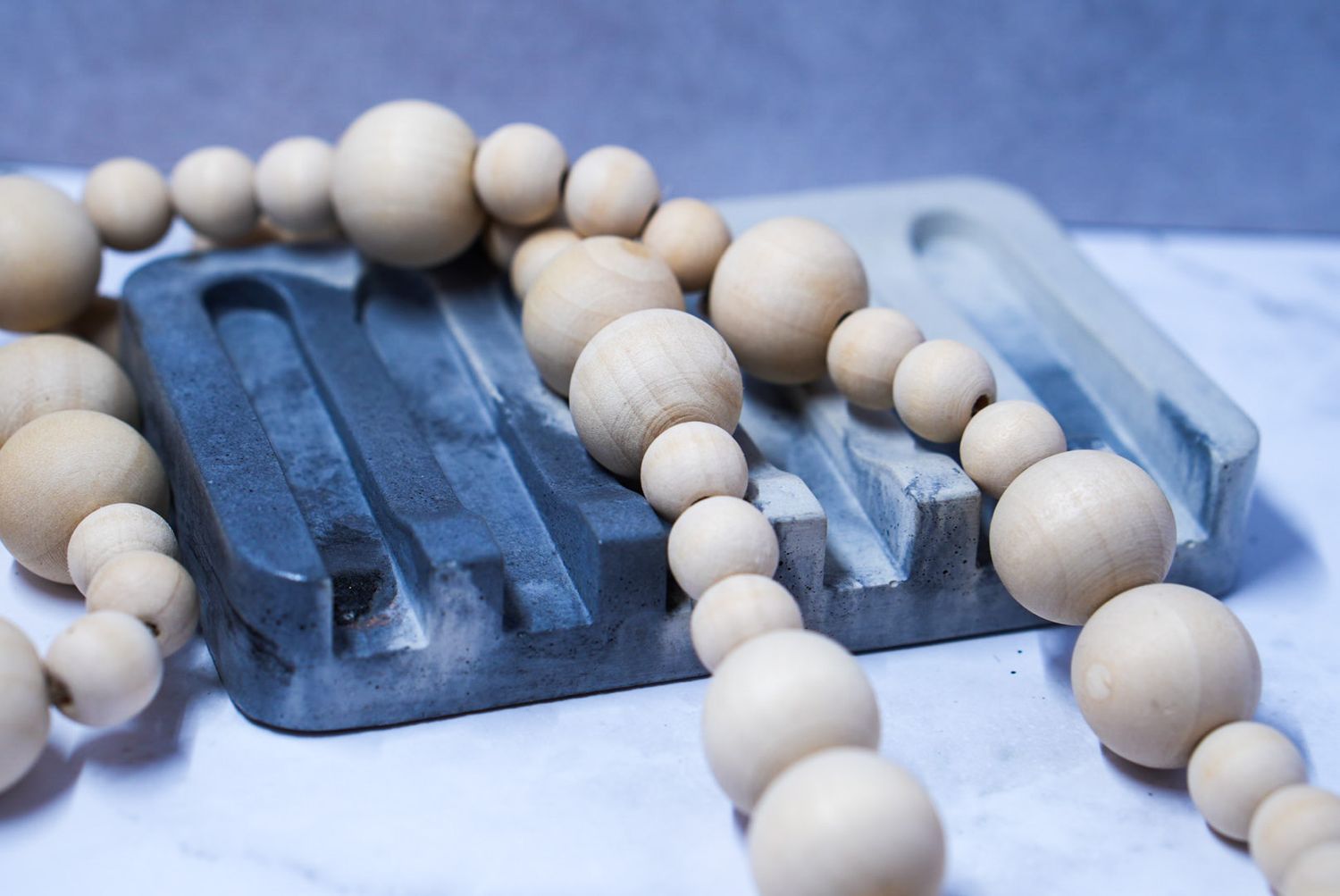 Wooden bead garland draped around two gray resin soap dishes on marble surface.