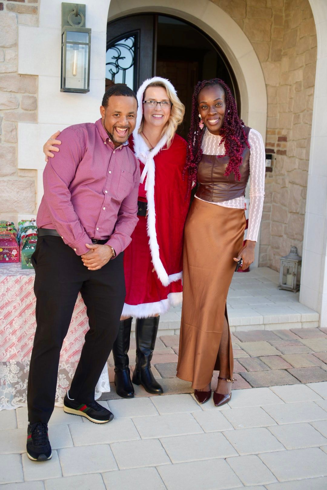 Three people pose together at front door, center person wearing red and white Santa Claus costume.