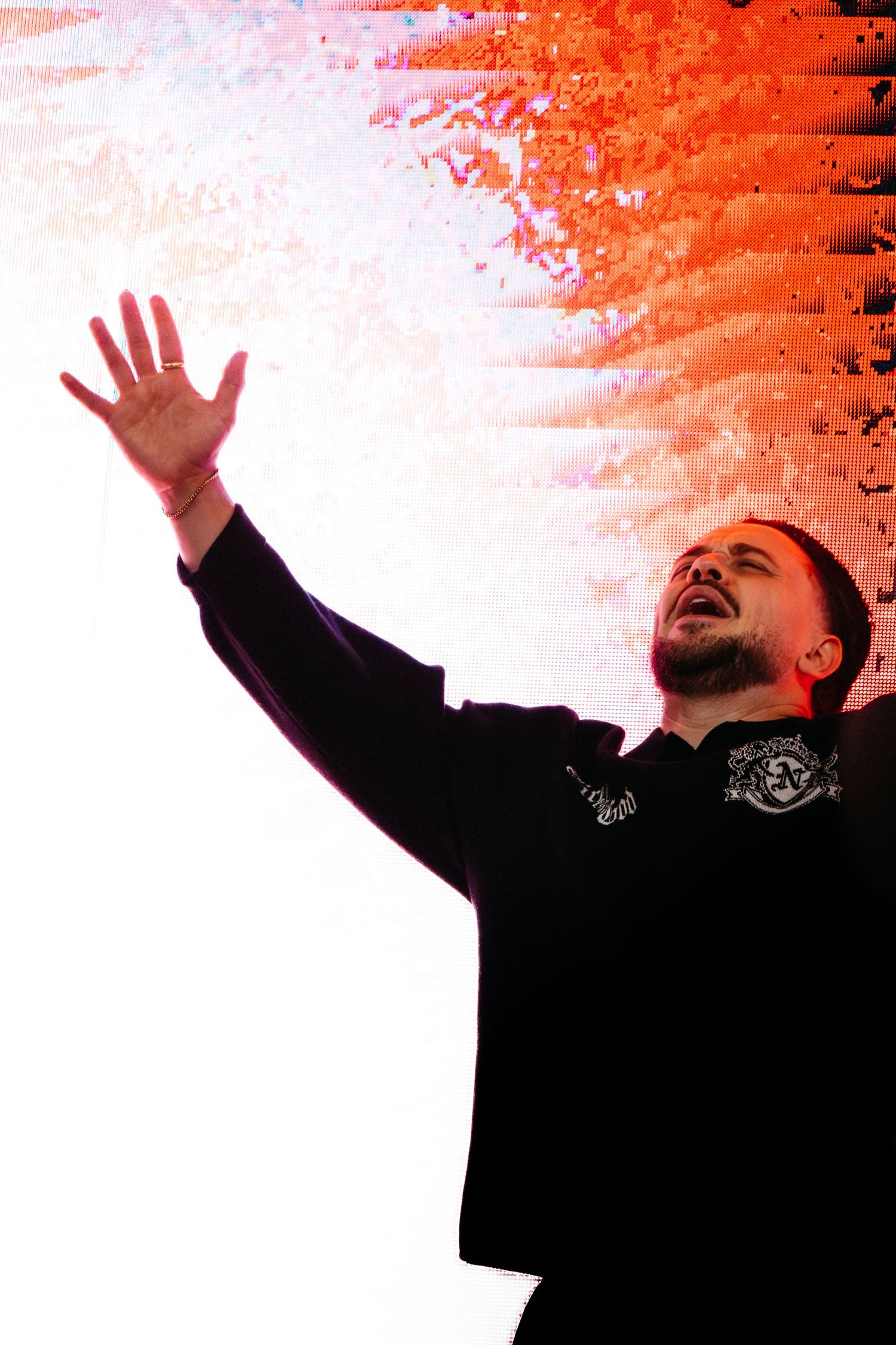 Male performer on stage raising one hand up with dramatic red and white lighting behind him.