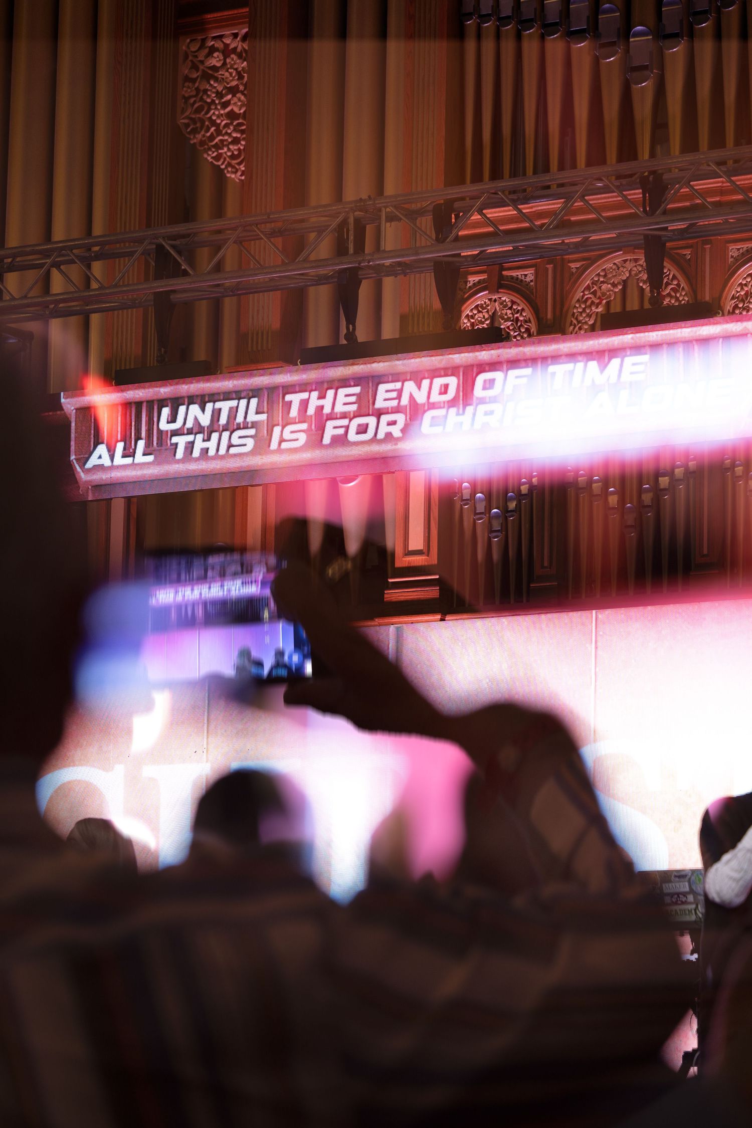 Crowd at a Christian worship concert with illuminated LED screen displaying lyrics in a grand hall.