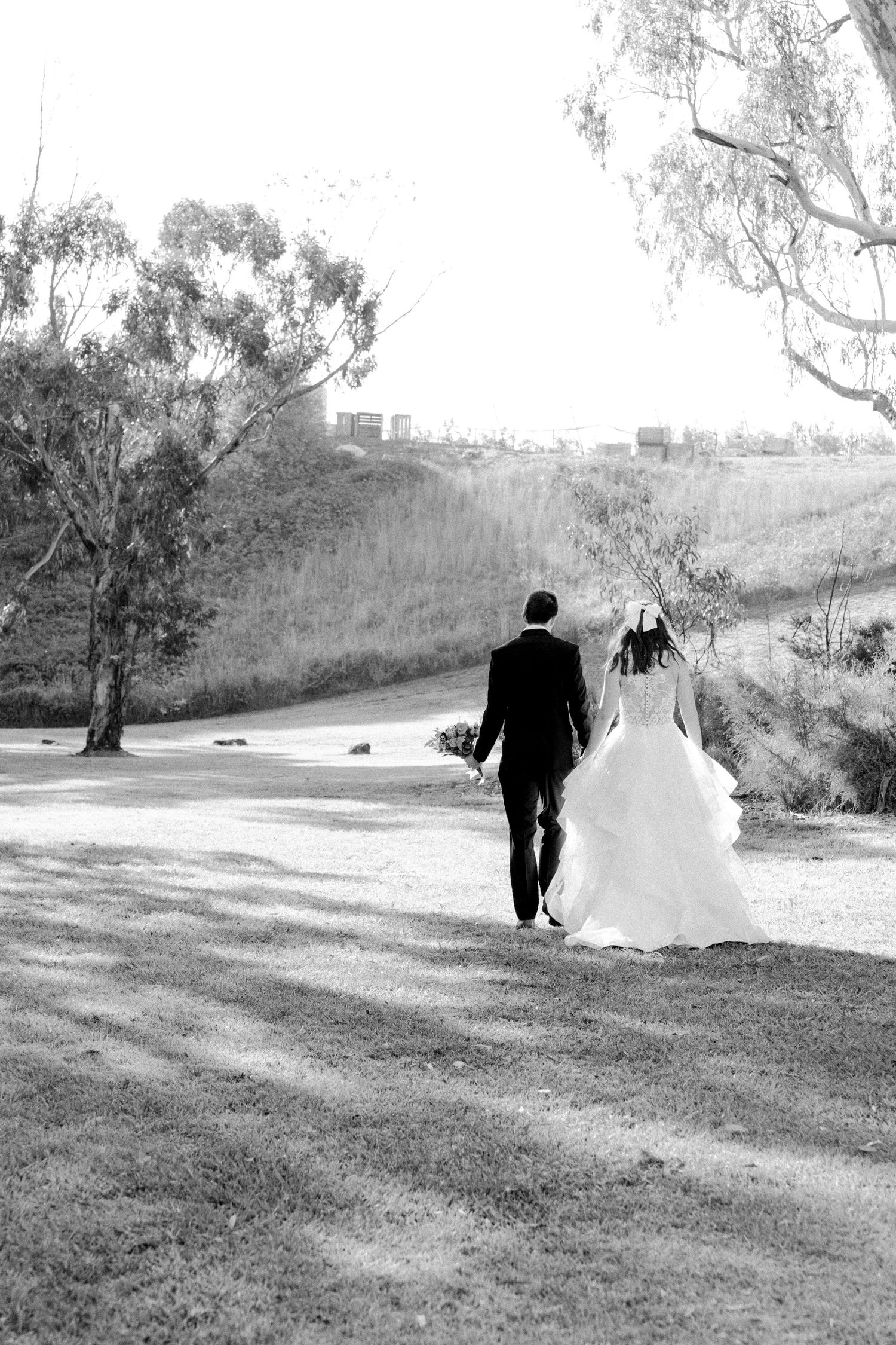 Bride and groom walk hand in hand through park in classic black and white photo.