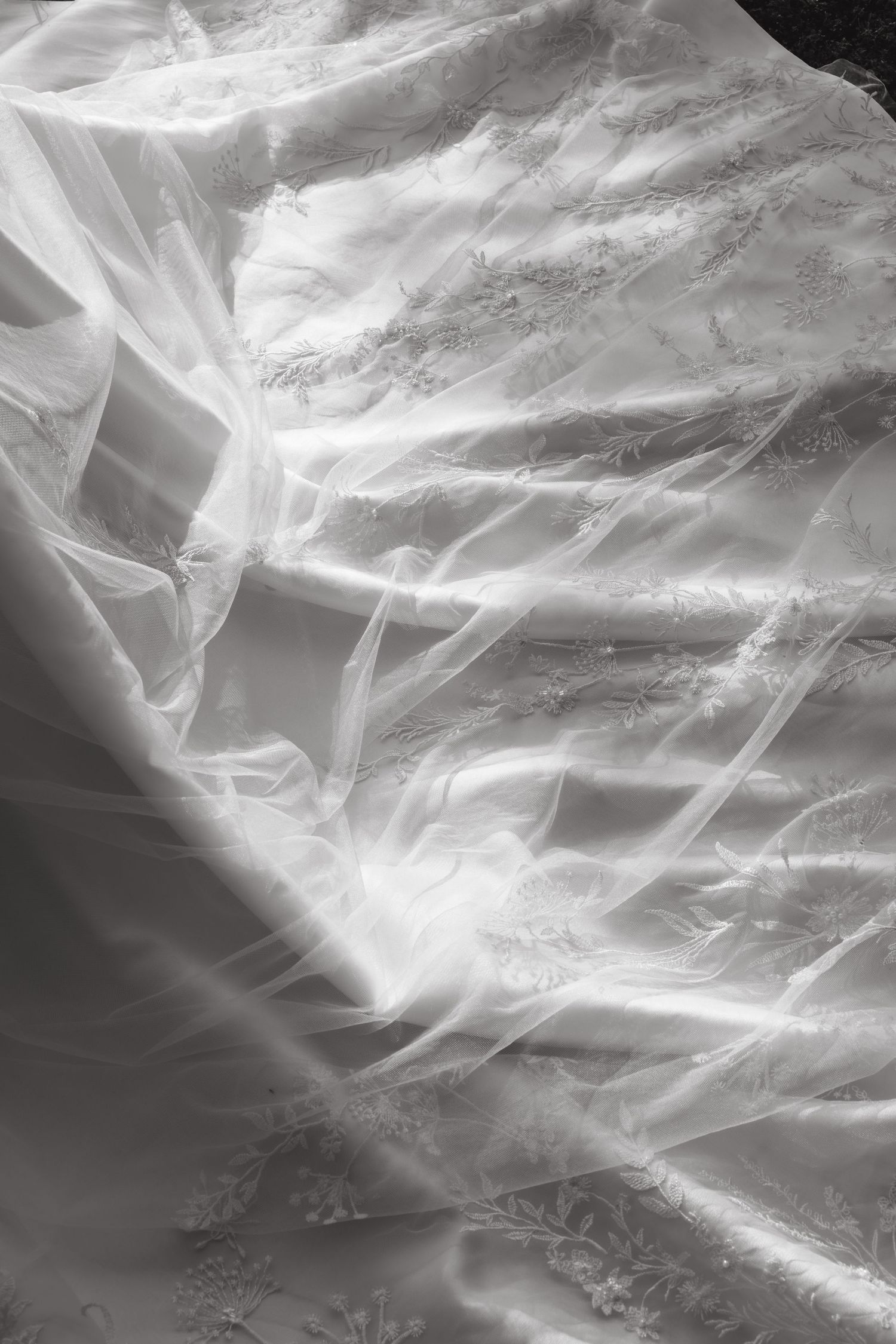 Close-up black and white photo of elegant wedding dress with delicate lace embroidery and flowing tulle layers.