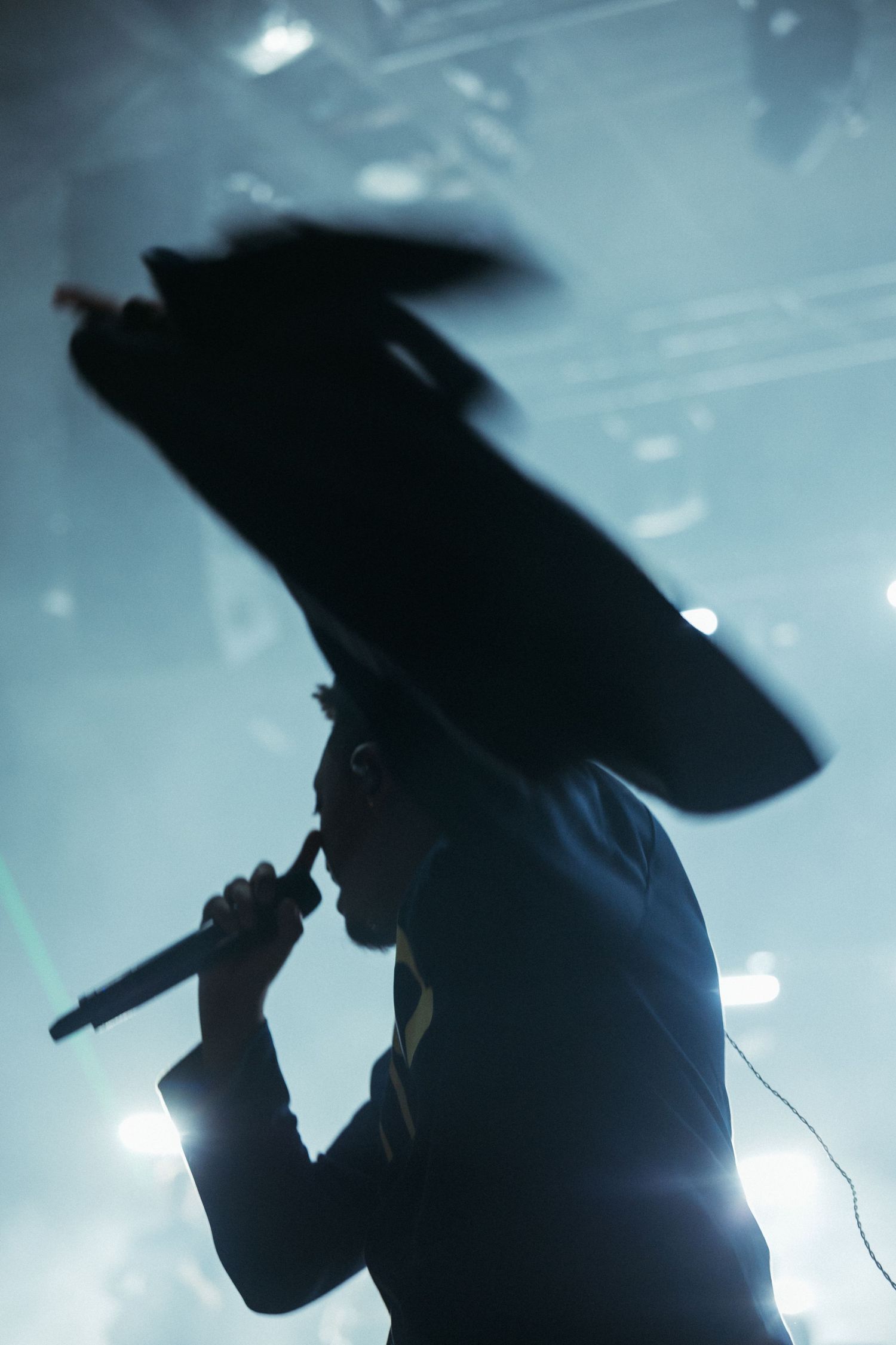 Silhouette of a performer singing into a microphone on a concert stage with dramatic blue backlighting.