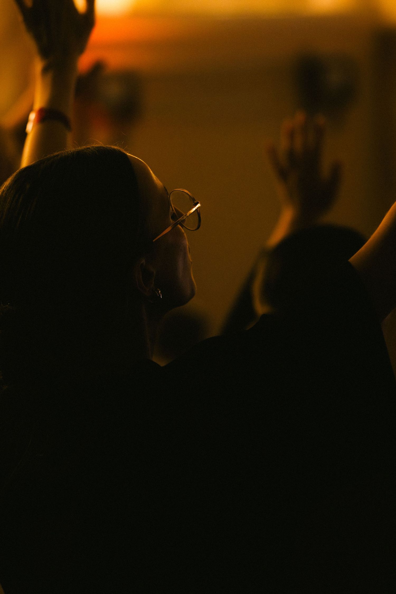 Woman with glasses raising hands in worship bathed in warm golden light.