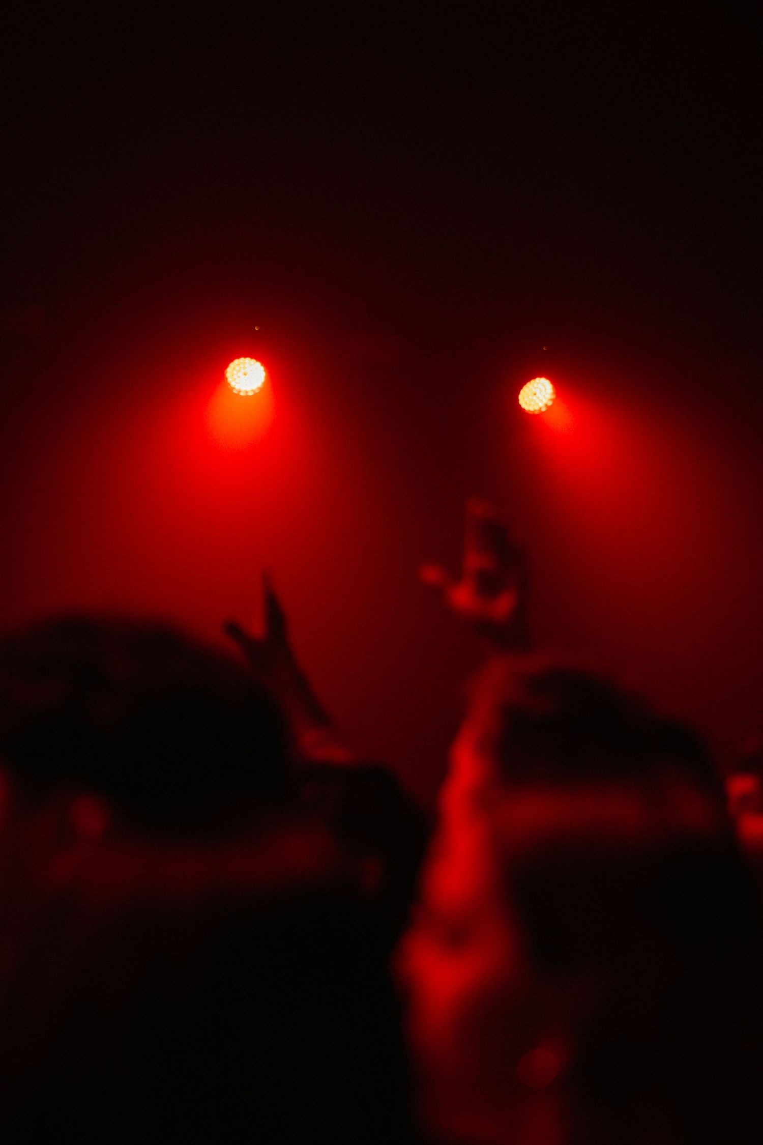 Crowd silhouettes raised hands under dramatic red stage lights at a concert event.