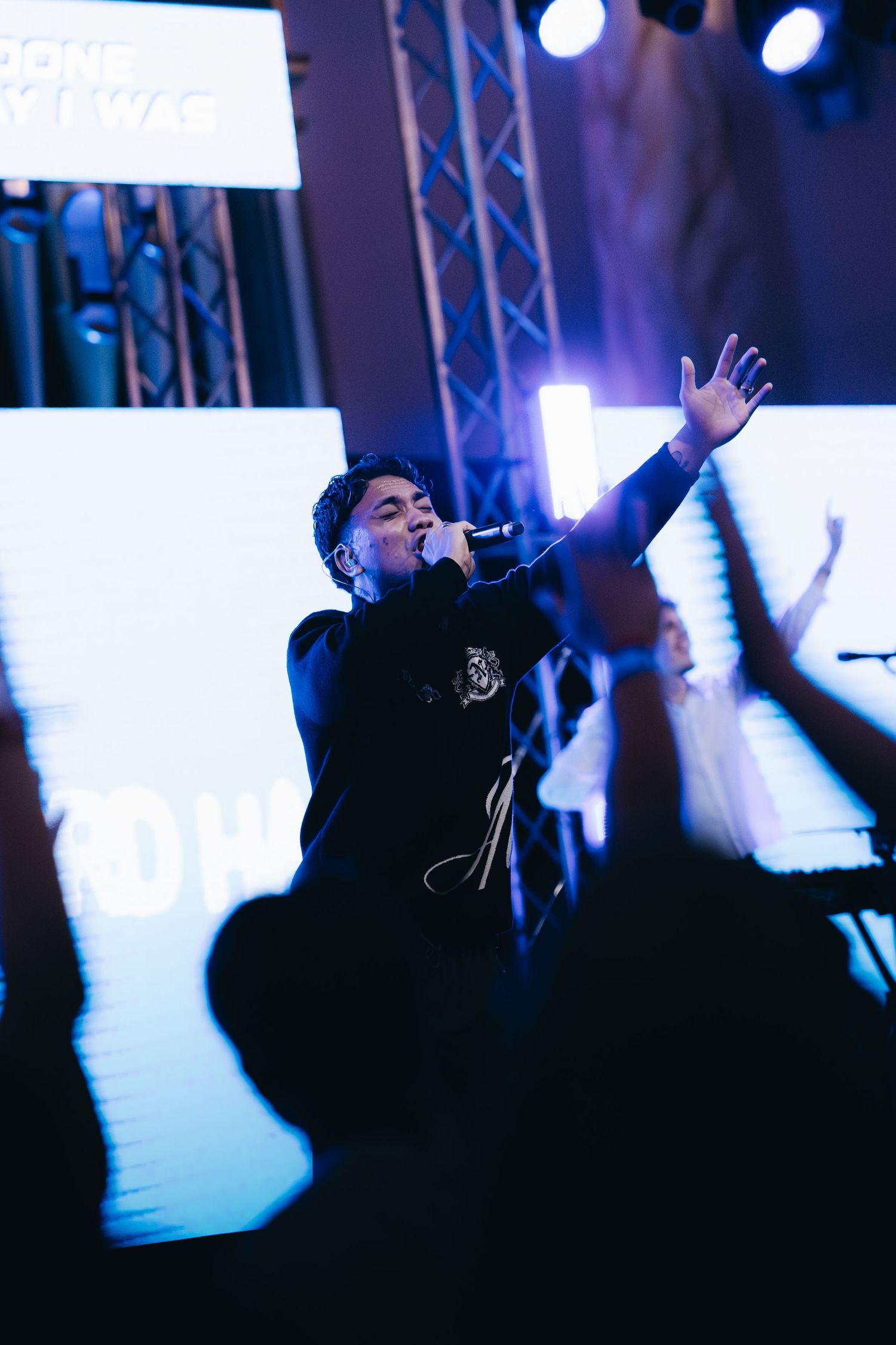Male vocalist sings passionately into microphone with one arm raised during a live worship concert.