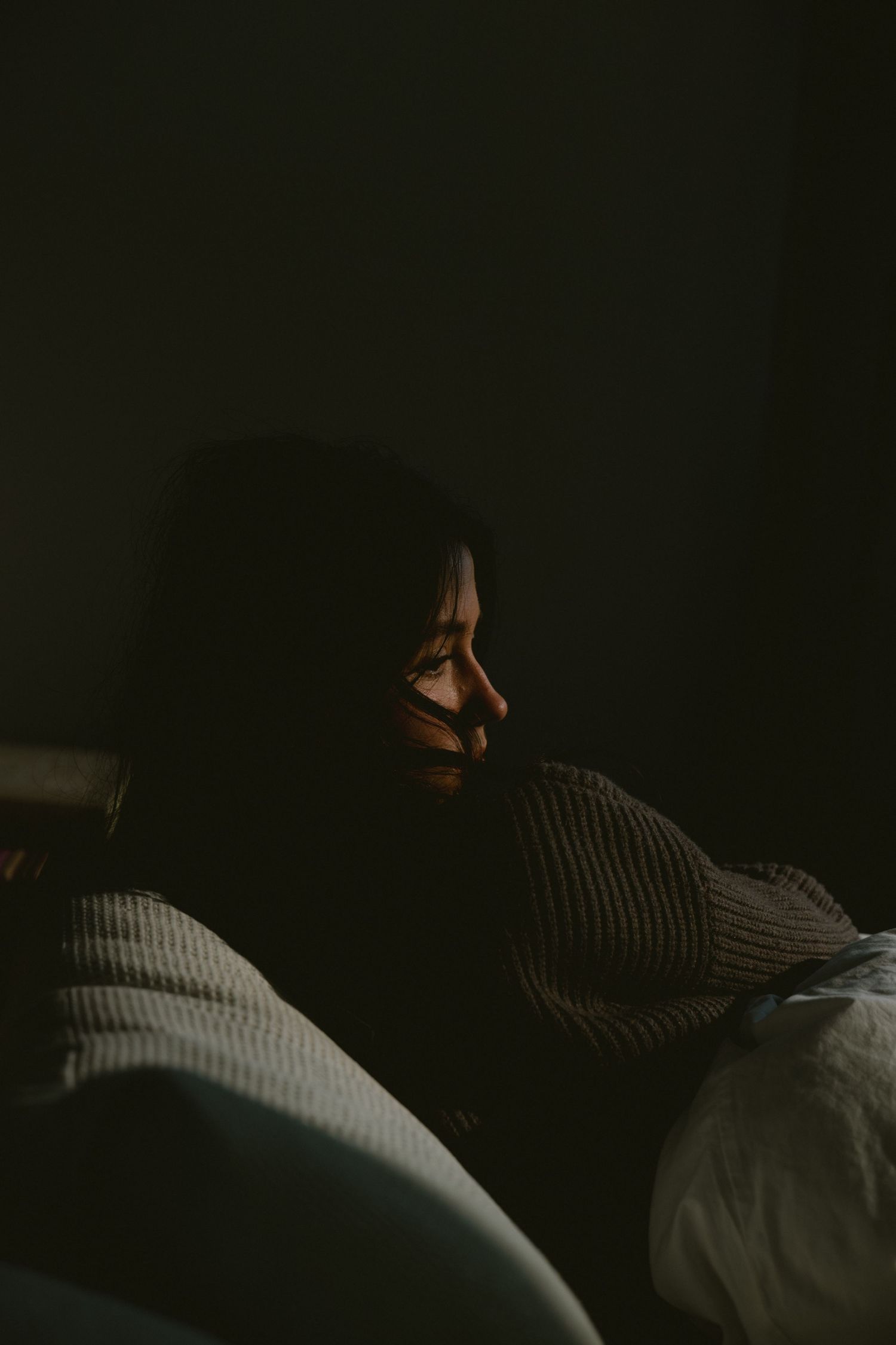 Woman in a striped sweater sitting in shadows, with dramatic side lighting on her face.