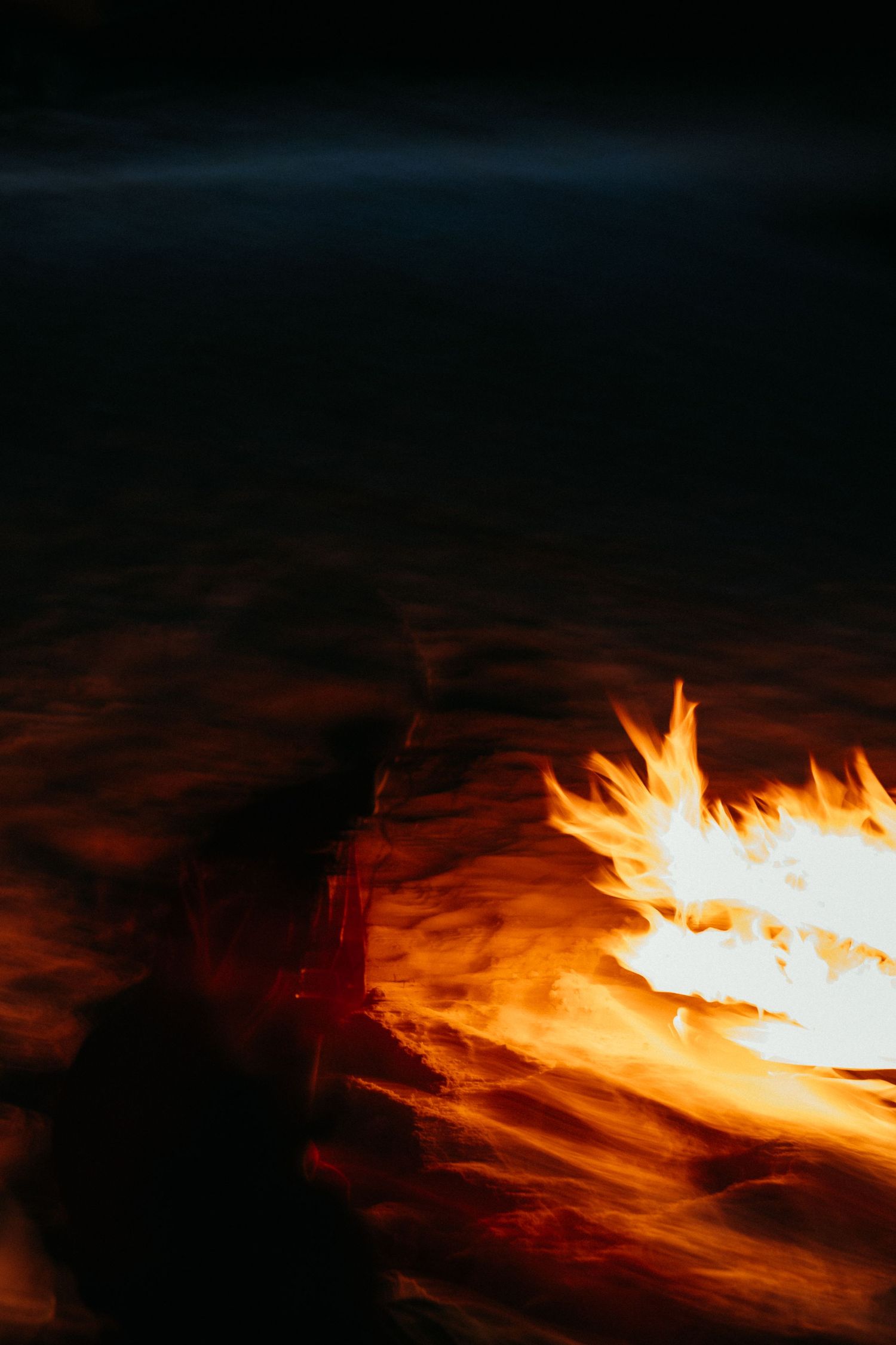A glowing campfire burning brightly on a dark beach at night with orange and red flames.