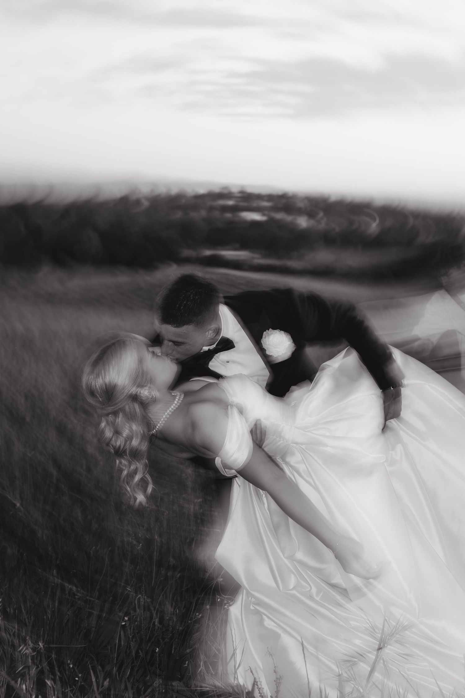 Black and white photo of a groom dipping and kissing his bride in a field on their wedding day.