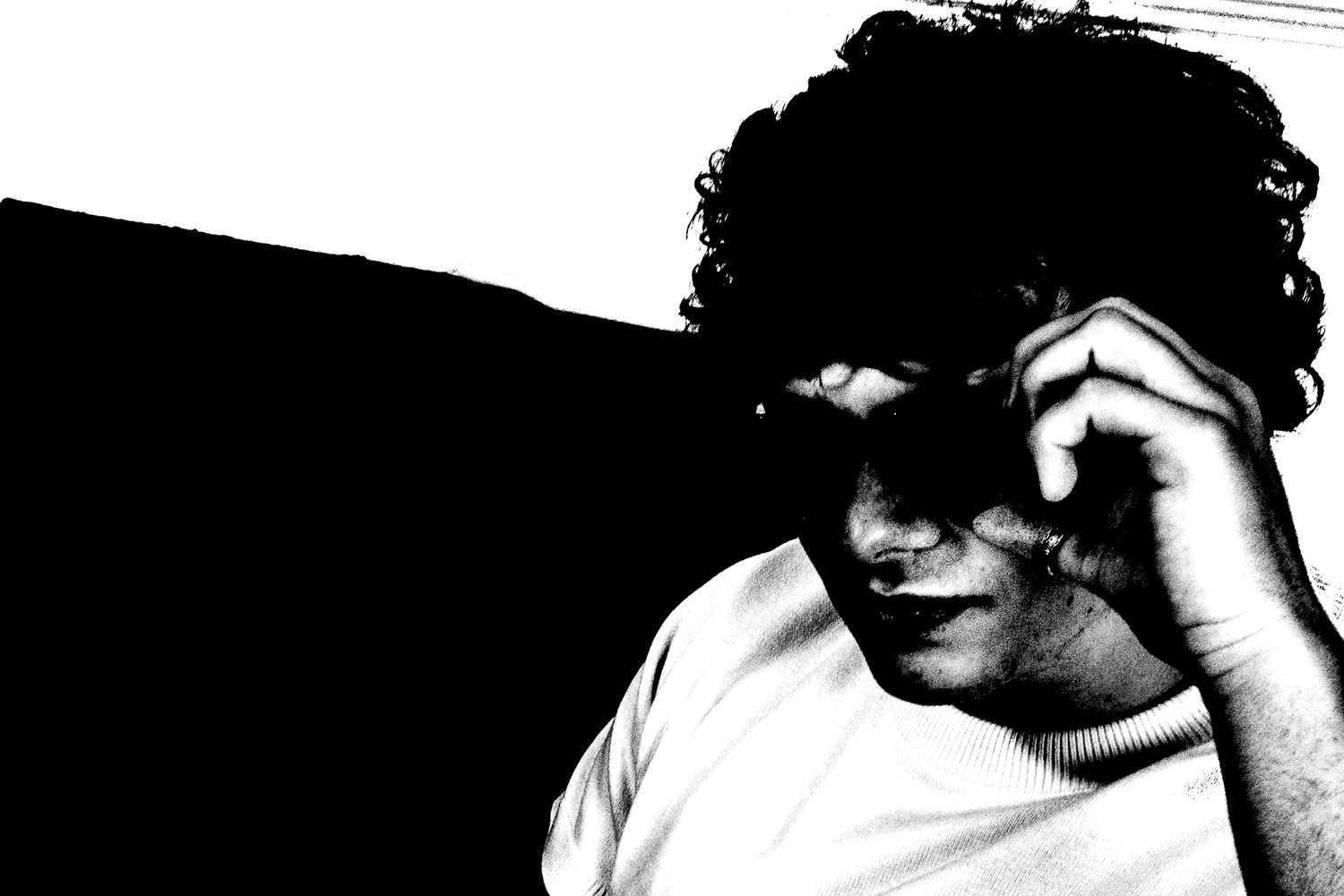 Black and white portrait of a young person with curly hair resting their hand near their face in dramatic lighting.