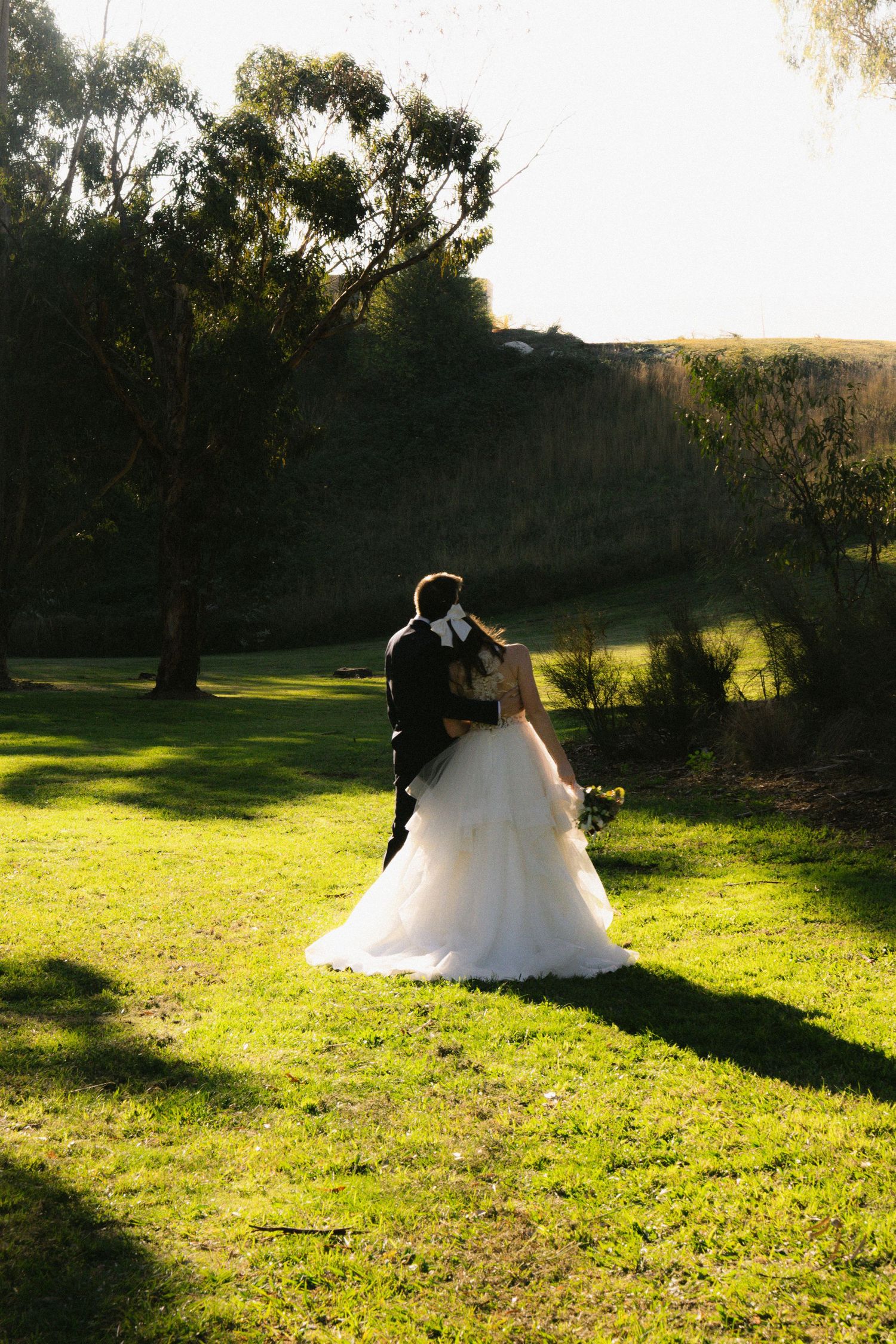 Bride and groom sharing a romantic kiss on lush green grass at golden hour in a scenic outdoor wedding.