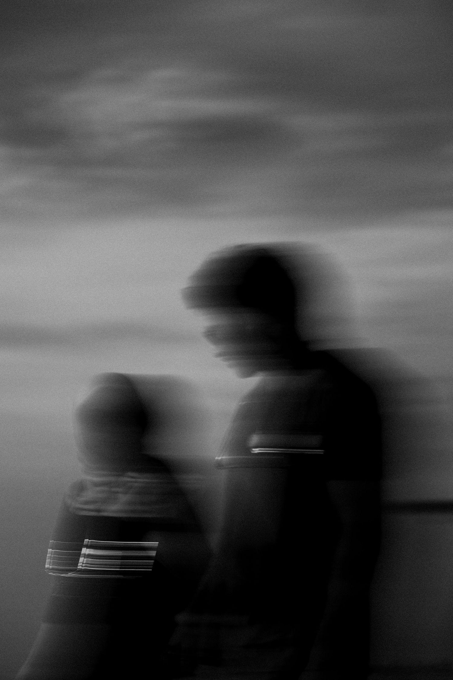 Blurry black and white motion blur photo of two people walking outdoors under a cloudy sky.