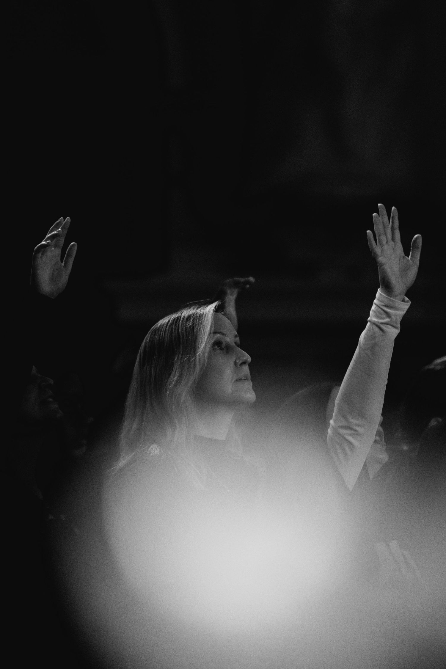 Black and white image of a woman raising her hands in worship at a live concert event.
