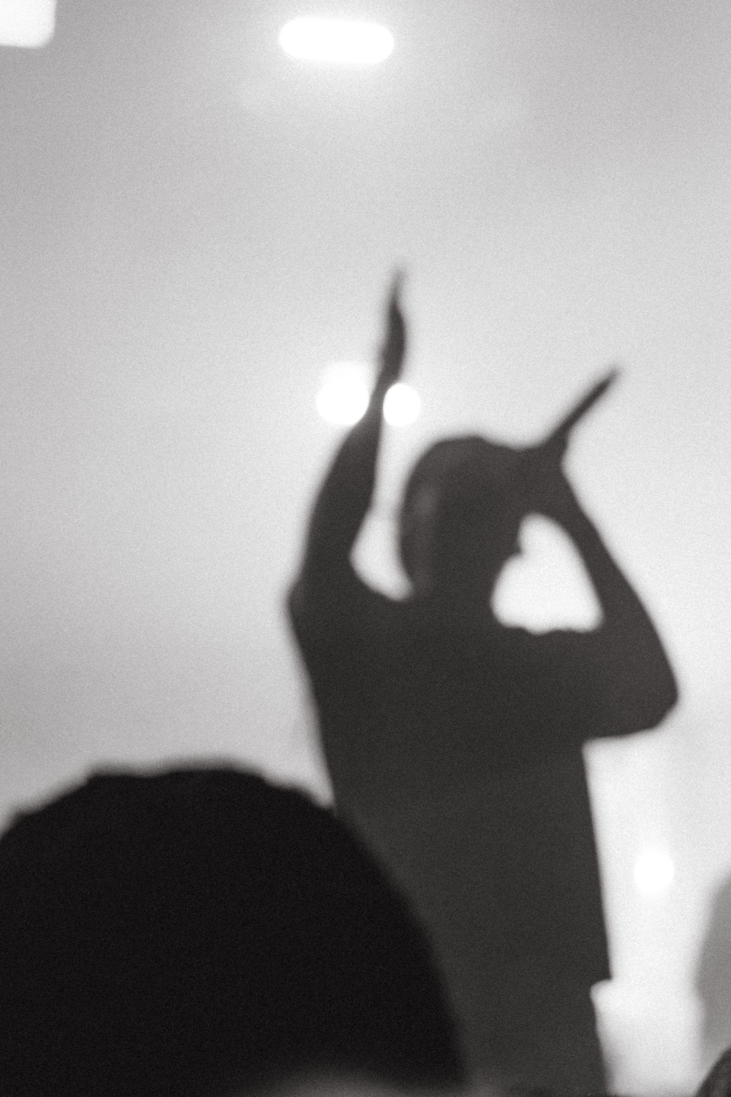 Silhouette of a performer holding a microphone with both hands raised under bright stage lights.