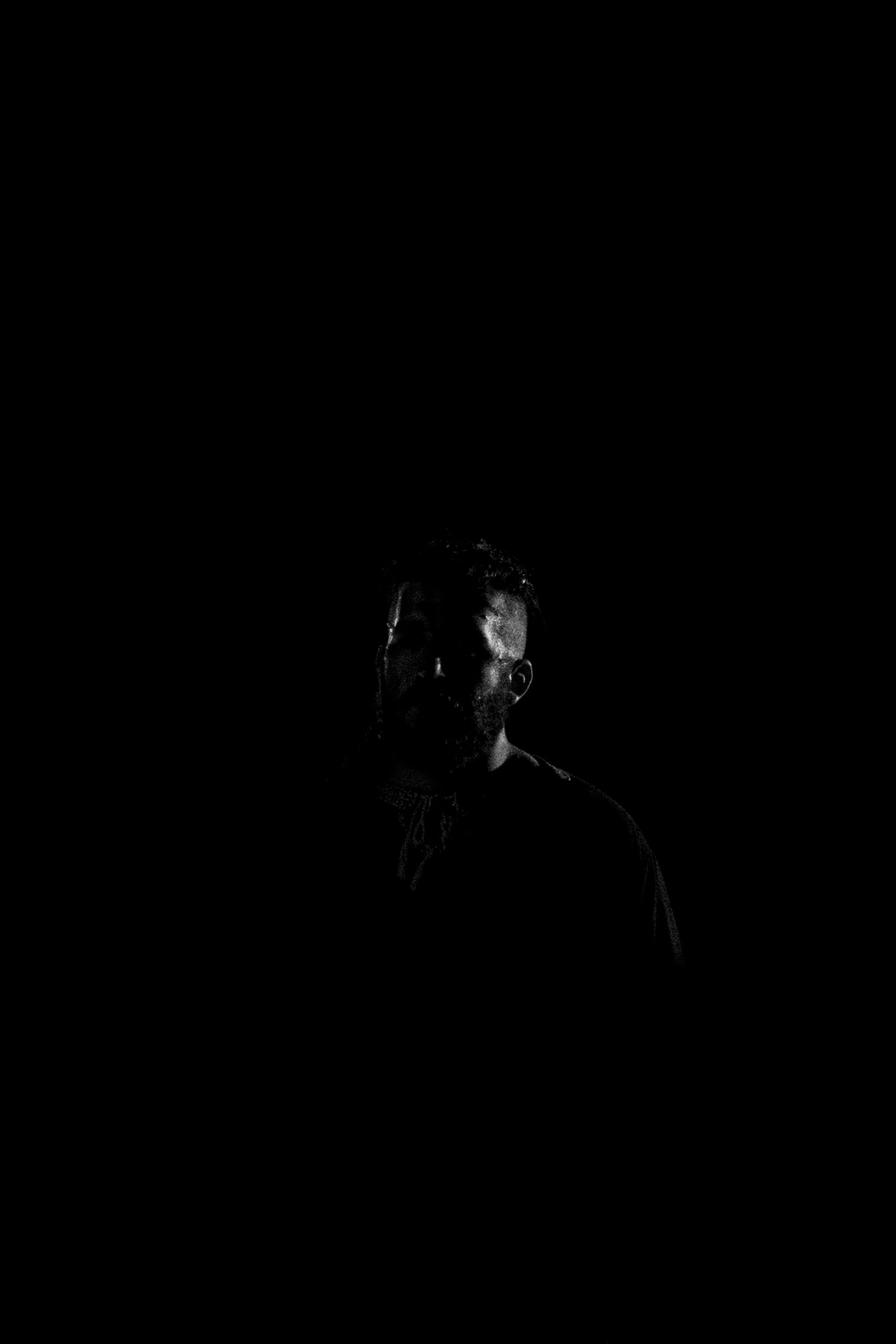 A mysterious man partially illuminated in darkness, dramatic low-key black and white portrait photography.