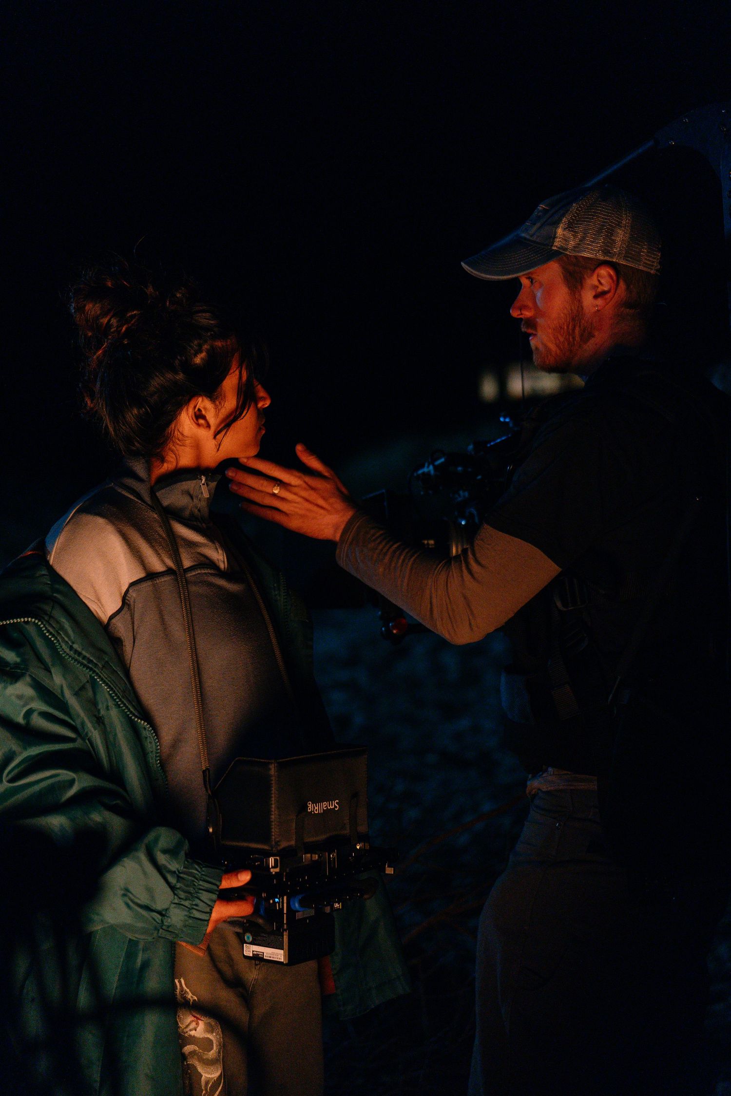 A filmmaker adjusts equipment on an actor during a nighttime film shoot on location.