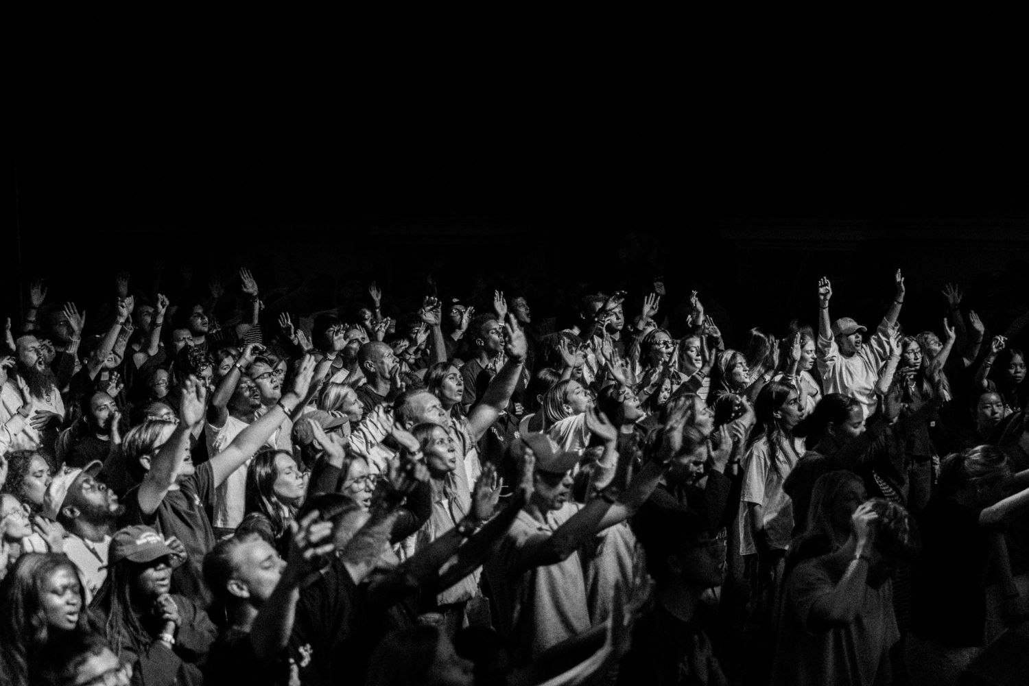 Black and white photo of a large crowd with hands raised at a live event.