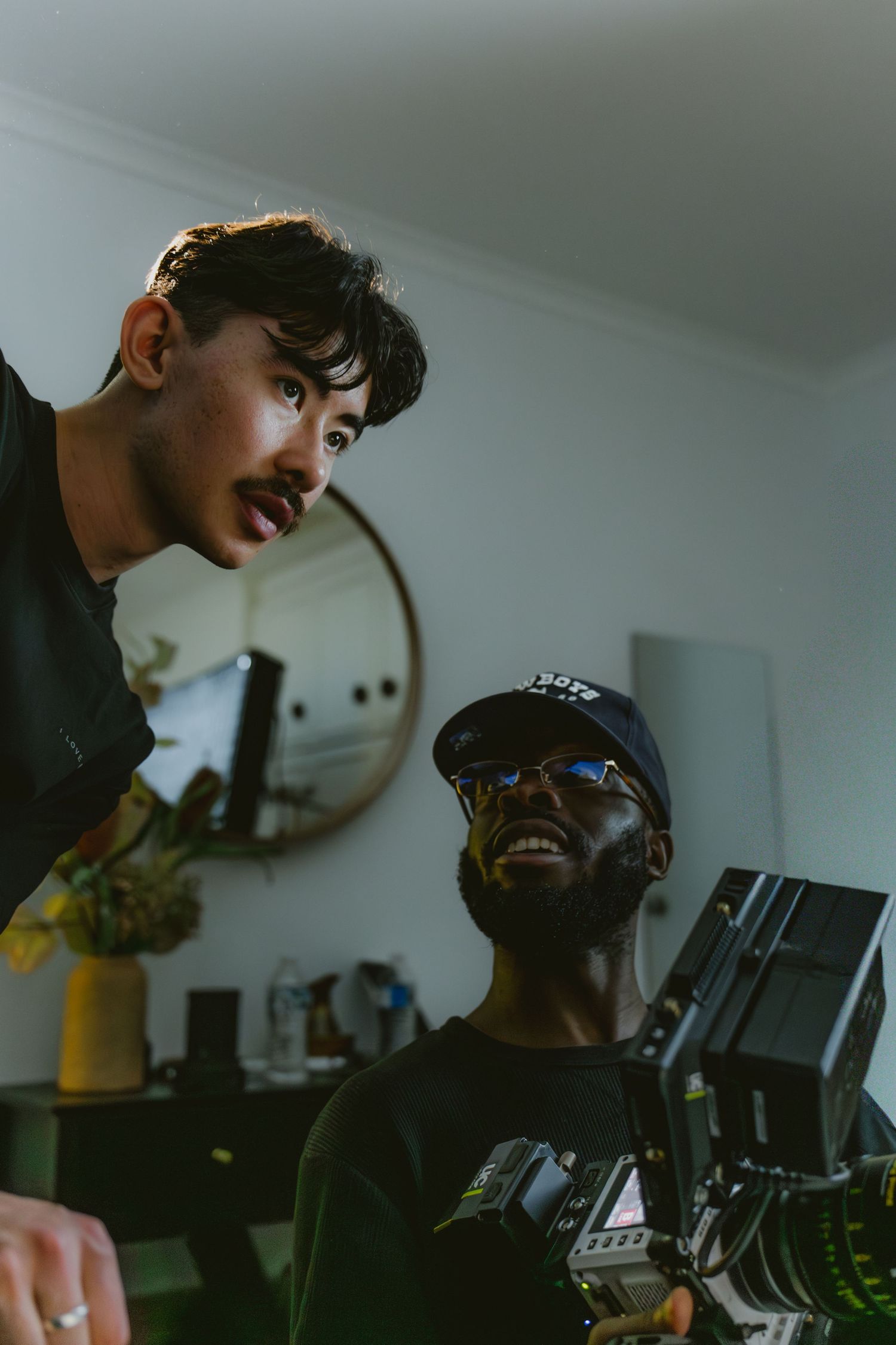Two young men examining a professional camera rig in a warmly lit indoor setting.