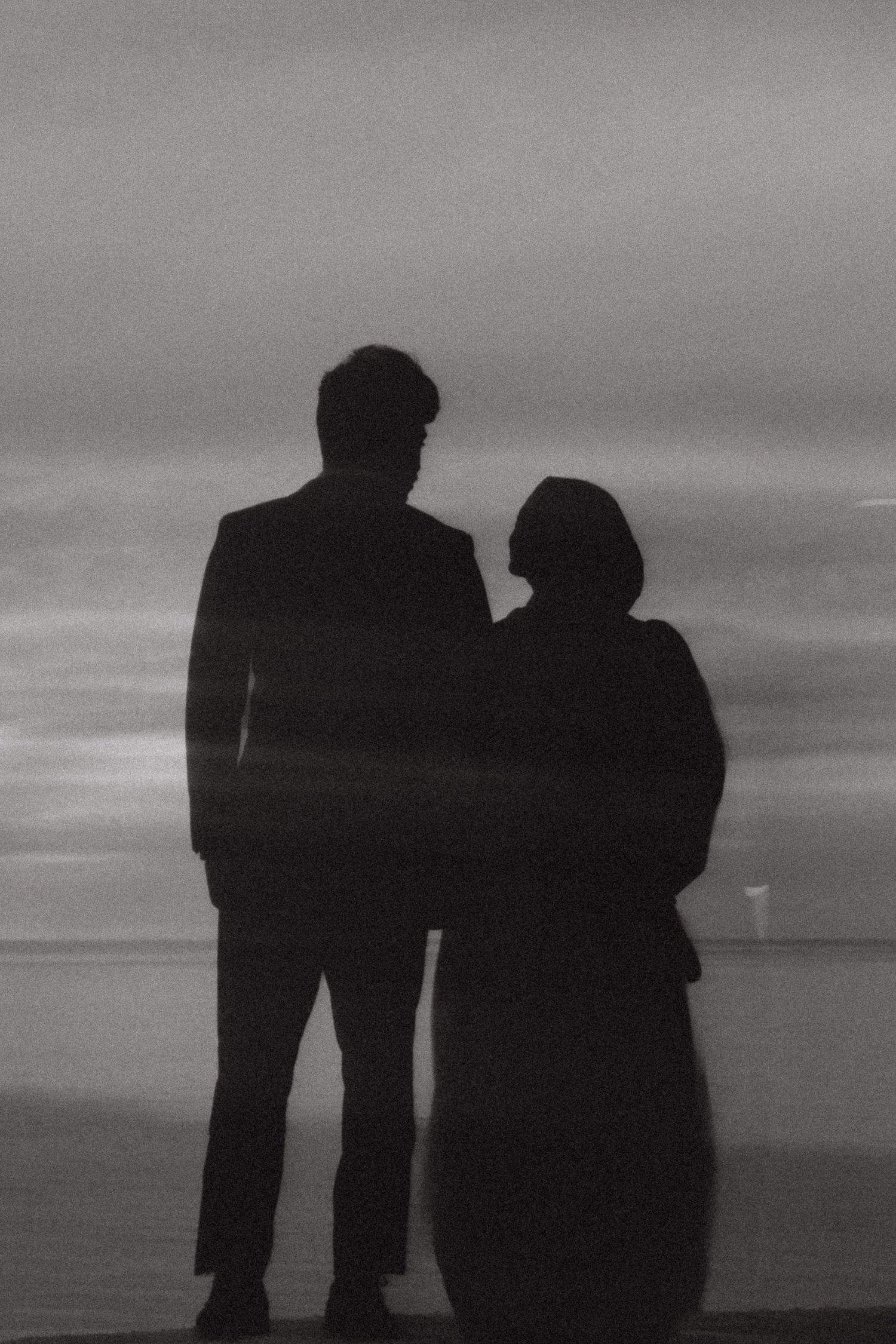 Black and white silhouette of a couple standing together by the ocean at dusk.