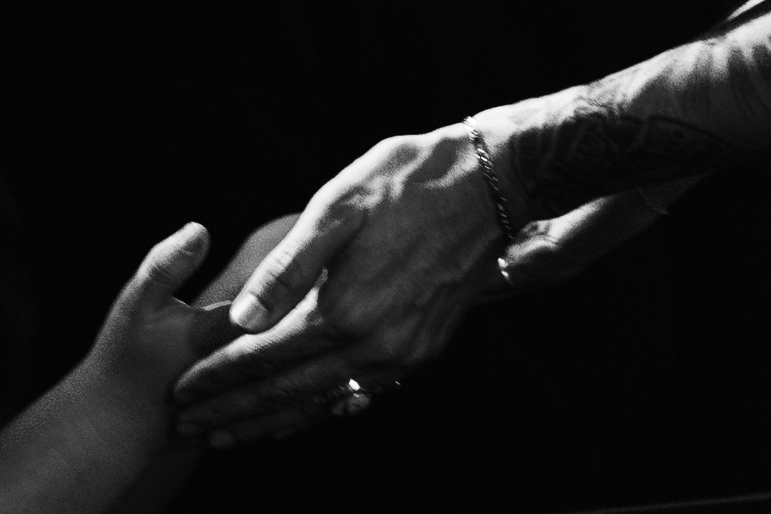 Black and white close-up of two hands clasping together against a dark background.