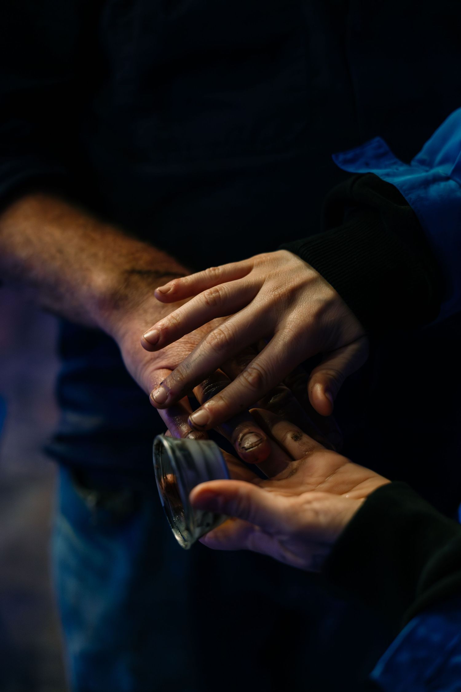 Close-up of two hands holding a small glass in dark blue dramatic lighting.
