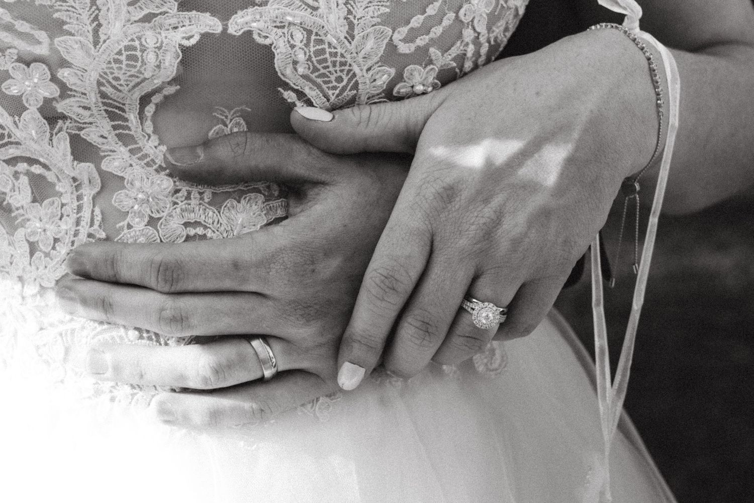 Close-up black and white photo of bride and groom wedding rings on lace dress.
