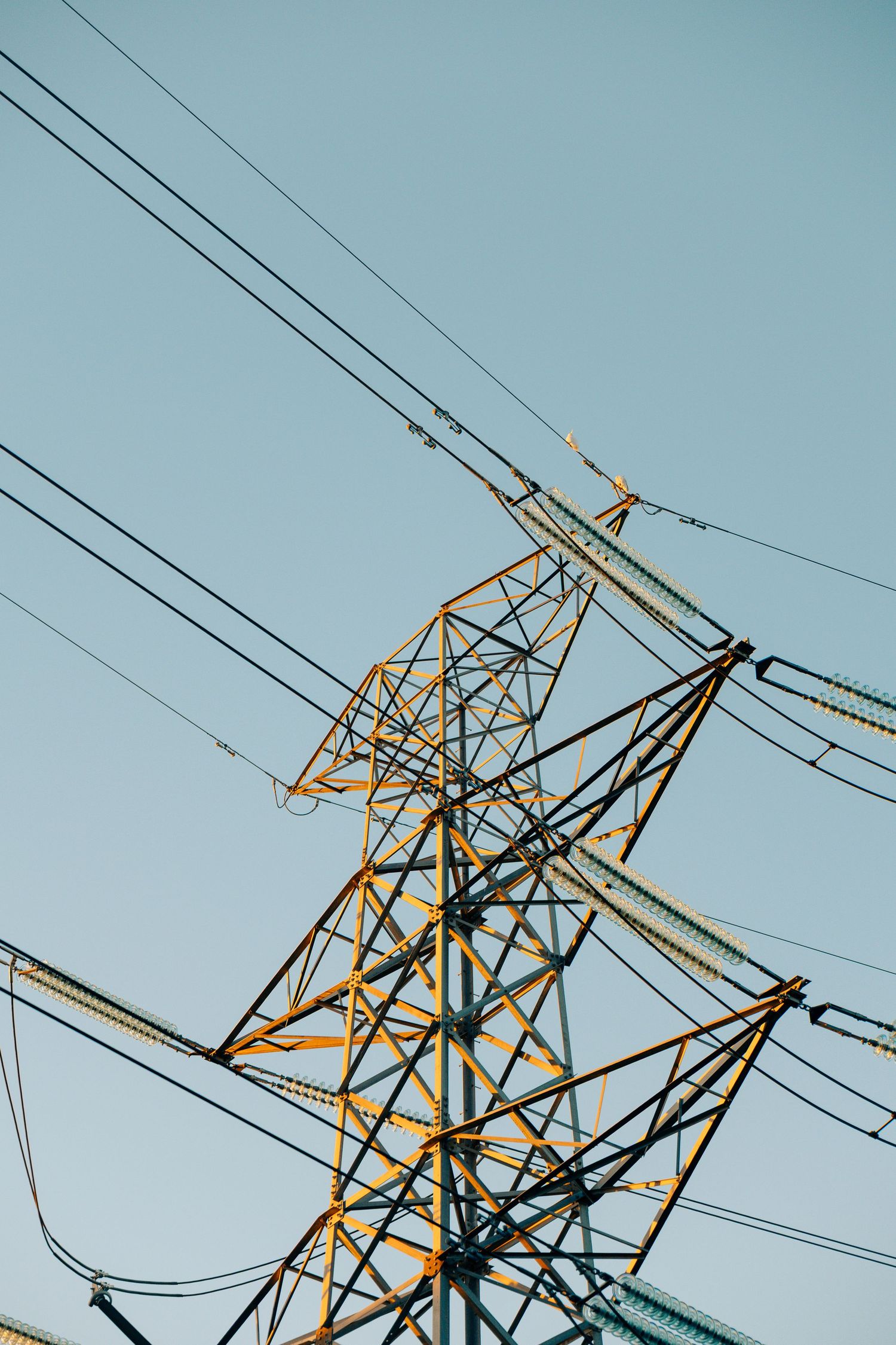Low angle view of a yellow steel electricity transmission tower against clear blue sky.