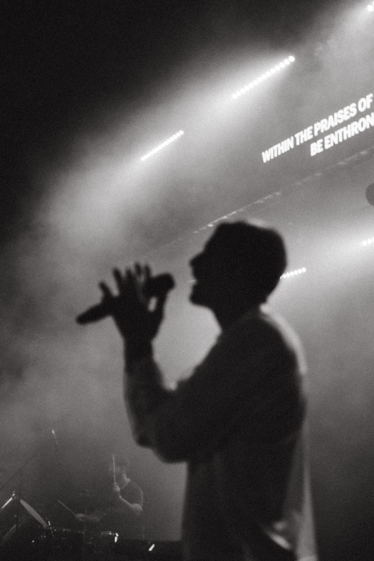 Silhouette of a singer holding microphone on stage with dramatic lighting and lyrics projected in background.